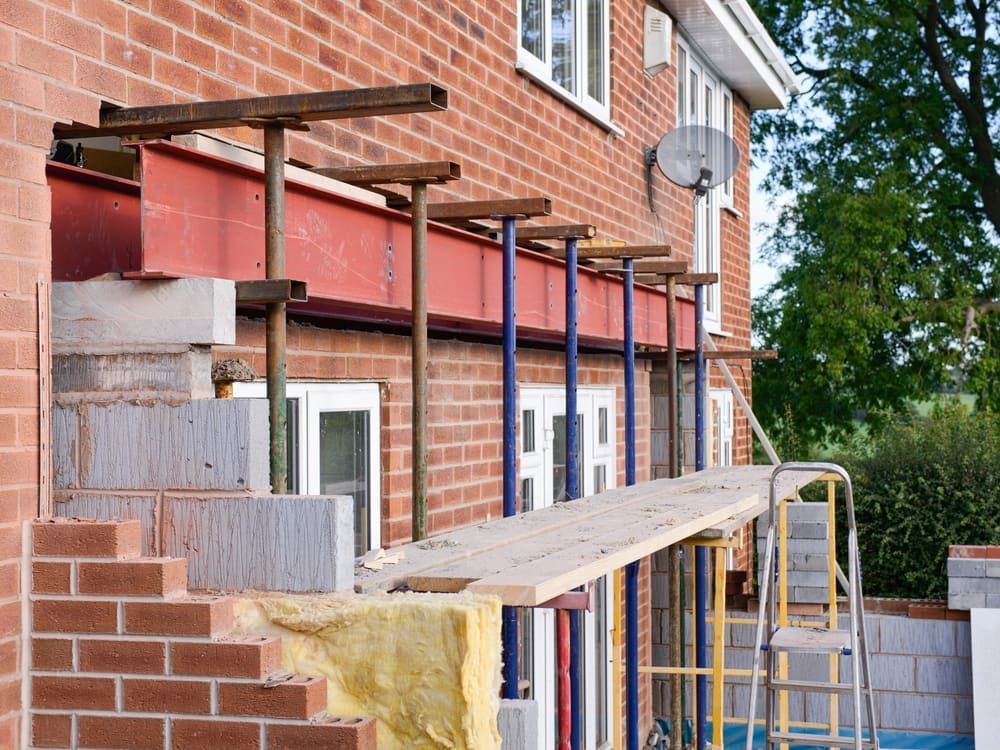A Brick House is Being Remodeled With Scaffolding and a Ladder — Ozi Construction Pty Ltd in Bondi, NSW
