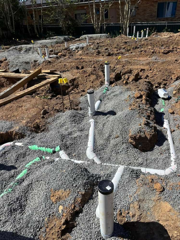 A Bunch of Pipes Are Laying in the Dirt on a Construction Site — Ozi Construction Pty Ltd in Wollongong, NSW
