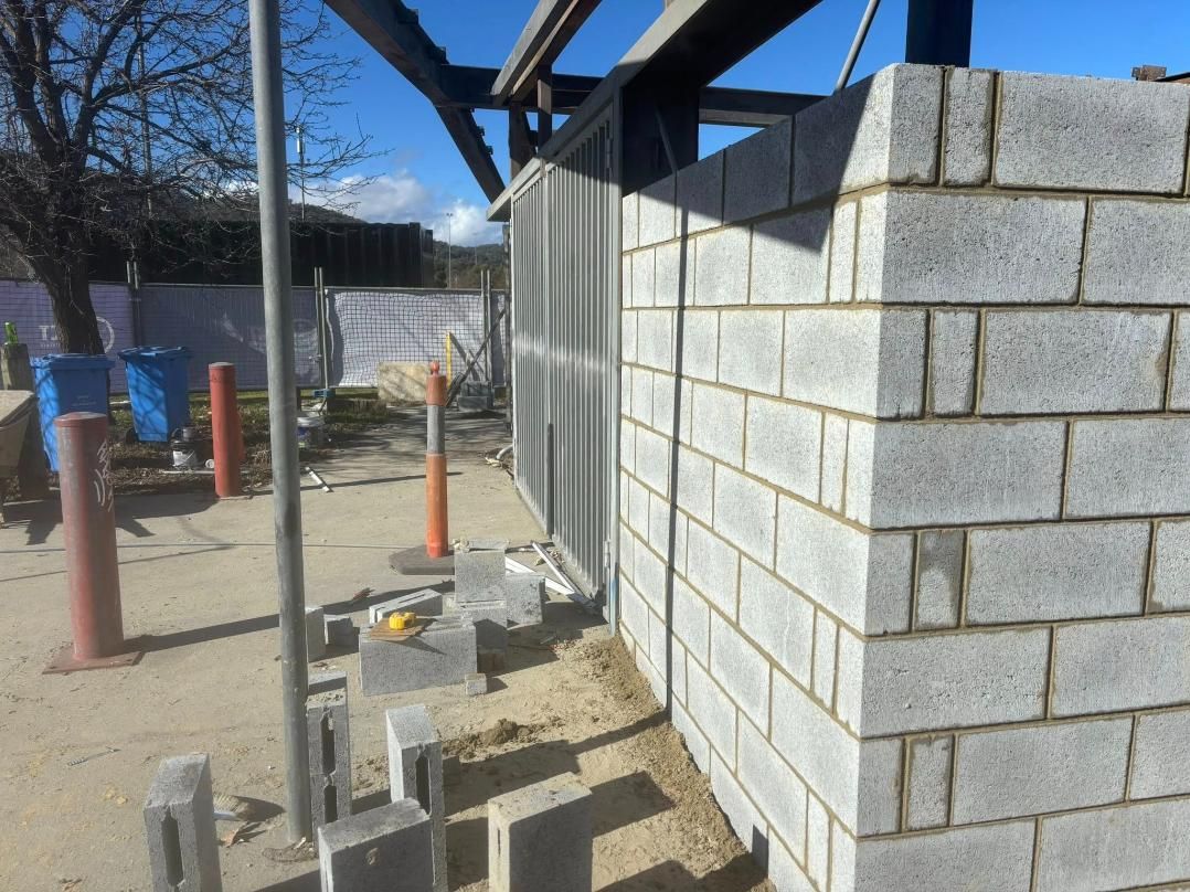 A Partially Built Brick Wall, Corner Visible, With A Metal Frame Above. Construction Site With Debris And A Cone