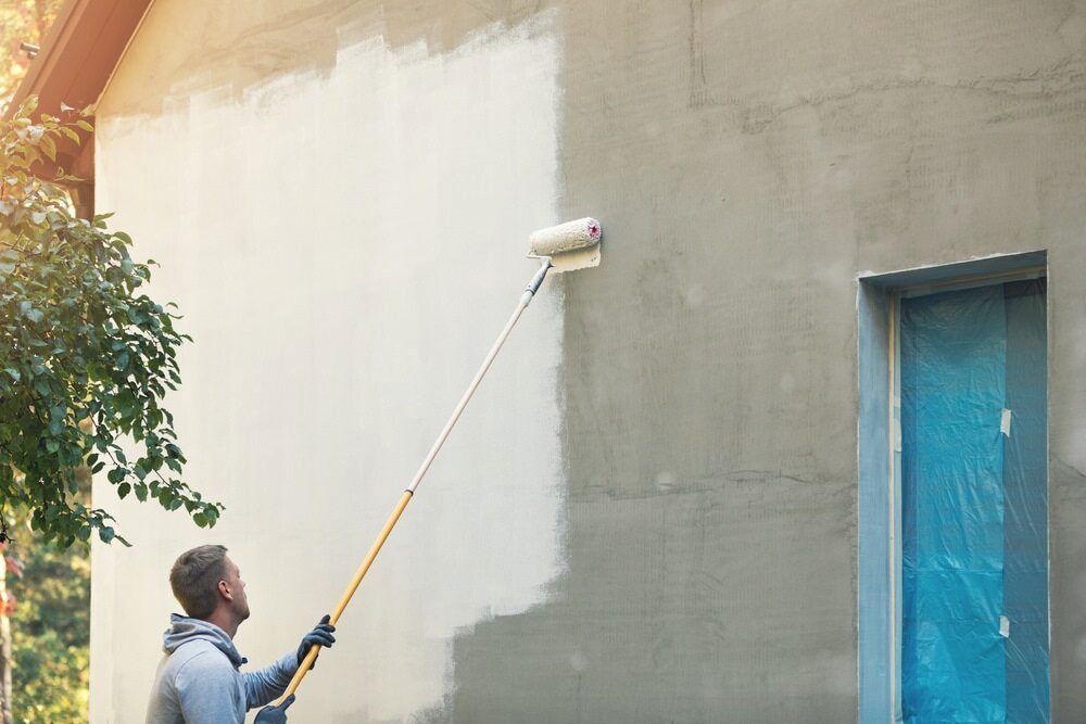 A Man is Painting a Wall With a Paint Roller — Ozi Construction Pty Ltd in Wollongong, NSW
