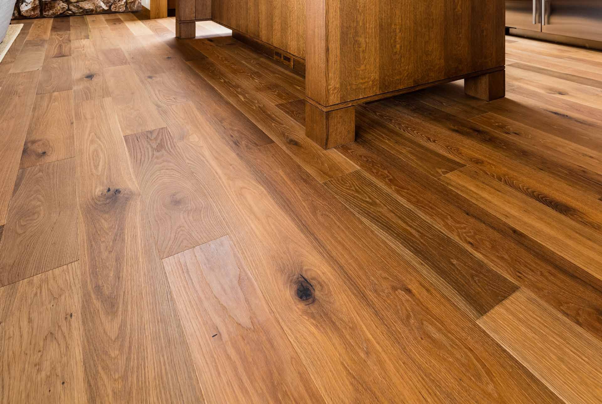 Wooden floor, light brown planks, beneath a dark wooden cabinet's base.