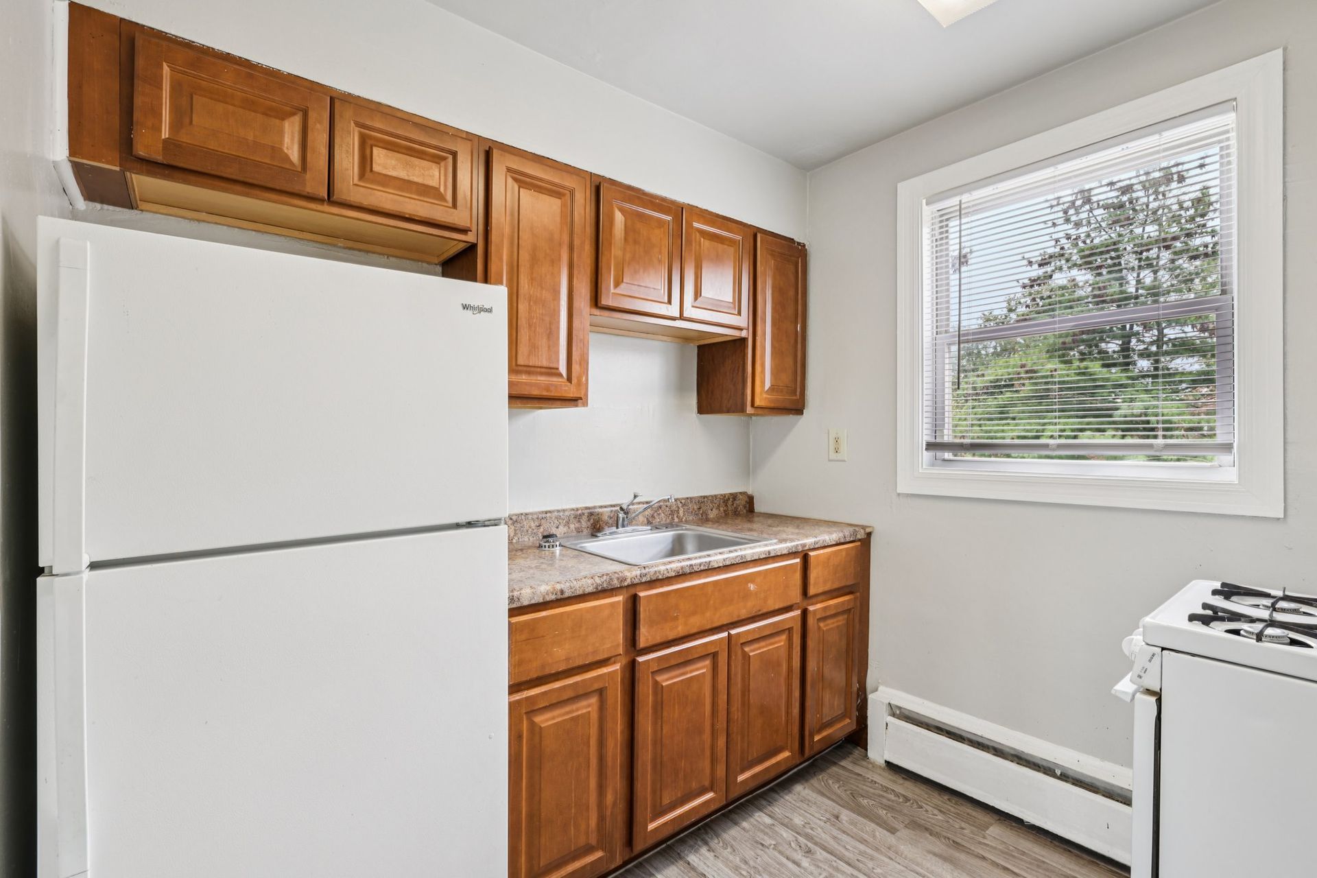 Small kitchen with wood cabinets, white appliances, and a window.