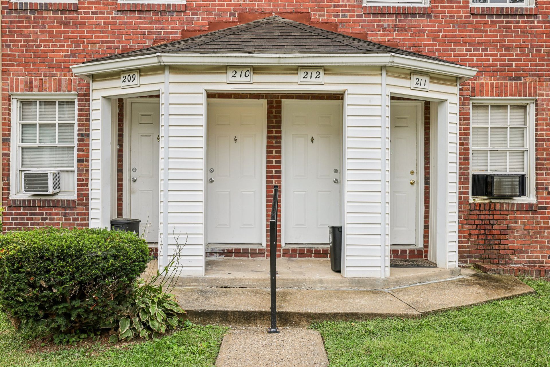 Apartment building exterior, brick and white trim, three doors under a covered entryway, green lawn.