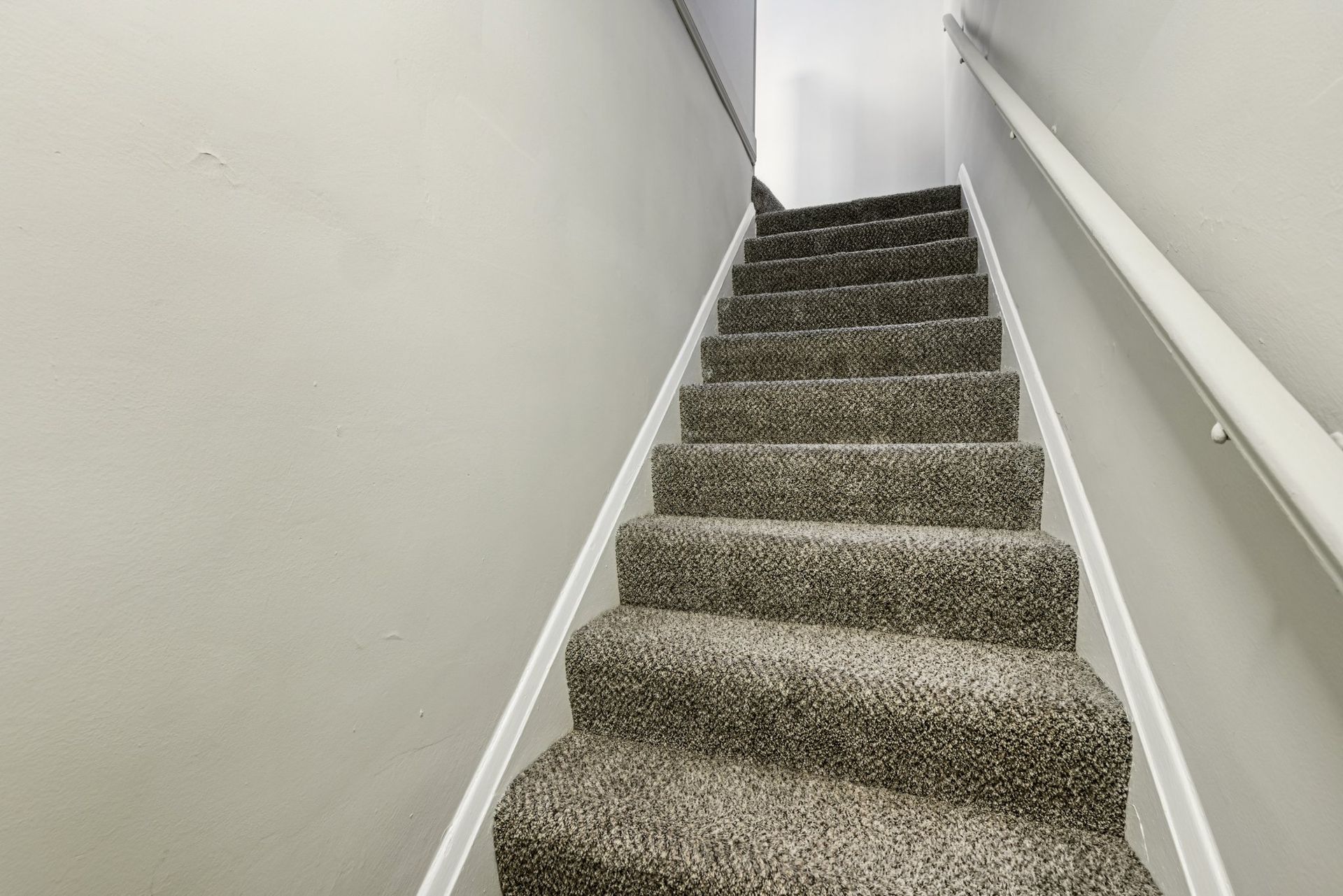 Staircase with gray carpet and white trim. Gray walls on either side with a white handrail.