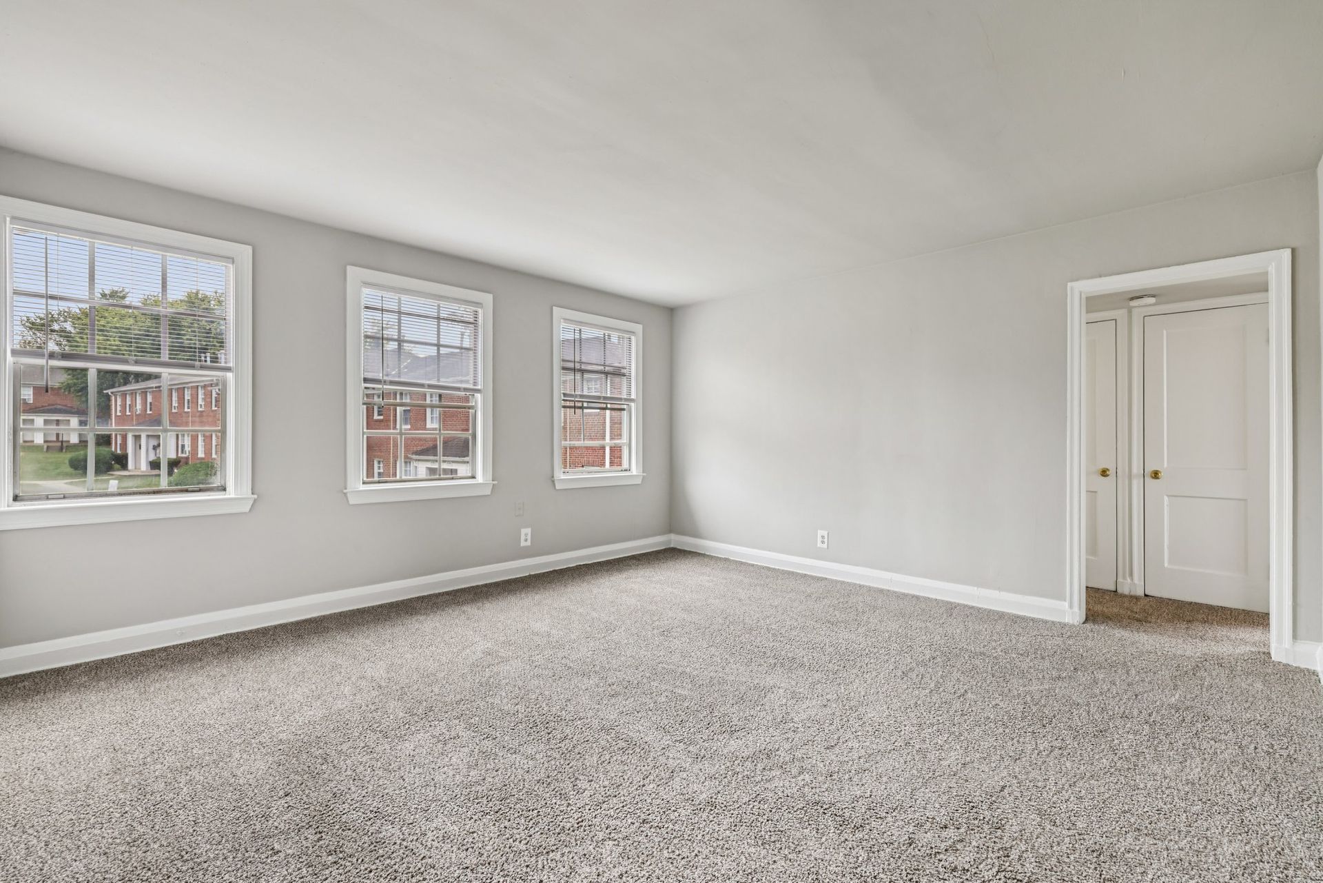 Empty room with three windows, two-door closet, gray walls, and light-colored carpet.