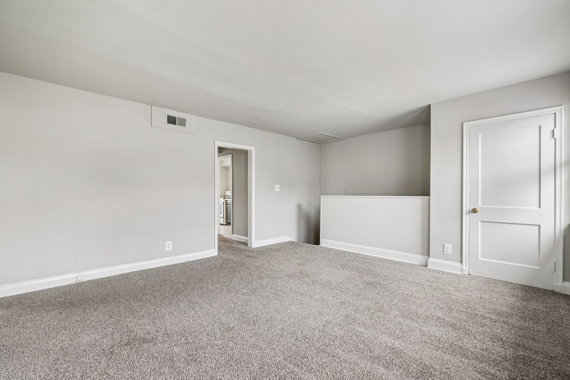 Empty room with gray walls, white trim, and a gray carpet. A white door is on the right.