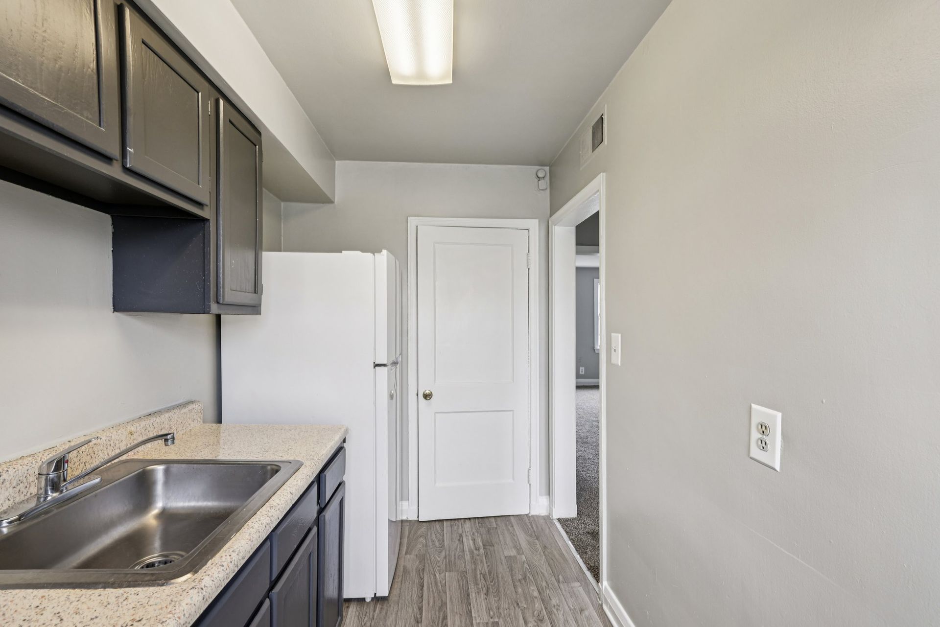 Kitchen with gray cabinets, white appliances, and a hallway leading to another room.