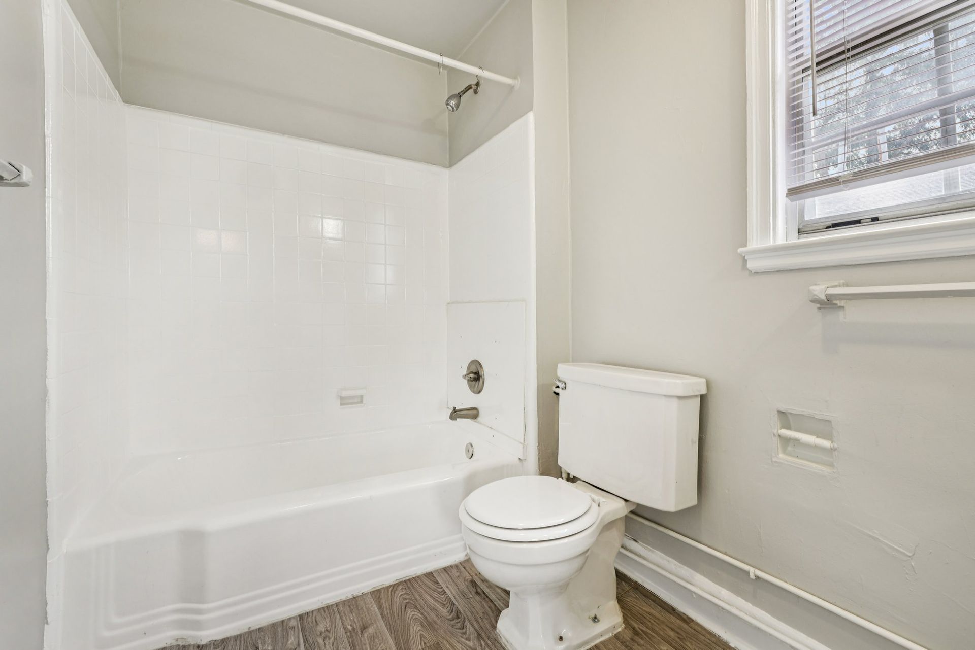 Bathroom with white tub/shower, toilet, window, and gray walls.