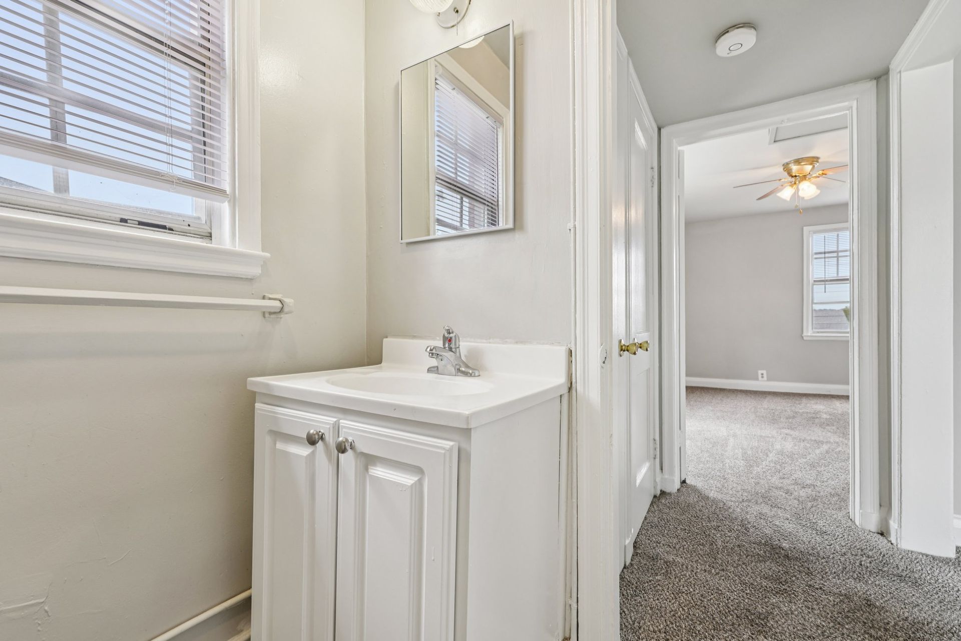 Small white bathroom with sink, mirror, and doorway to a bedroom.