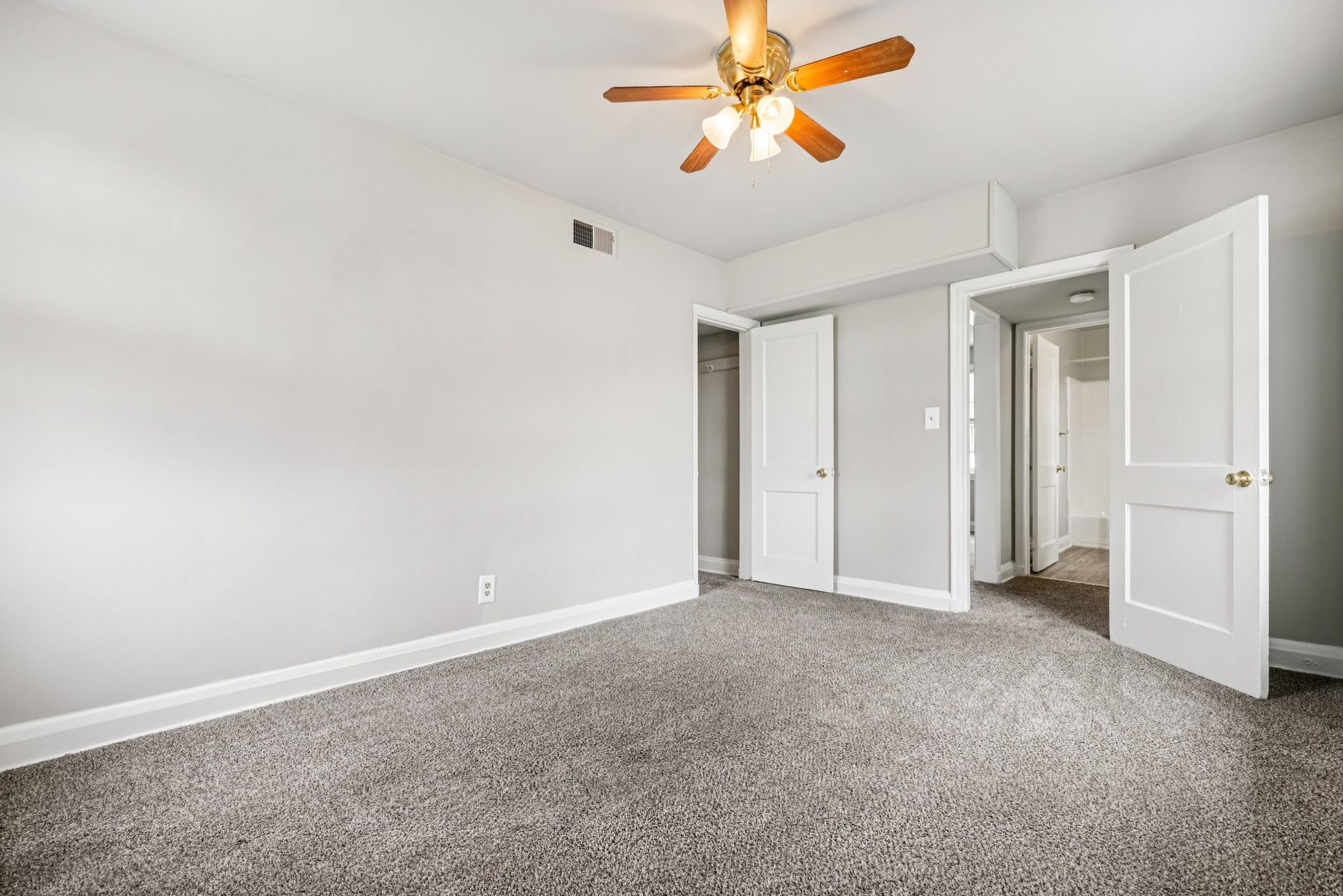 Empty bedroom with gray walls, carpet, ceiling fan, two white doors, and a closet.