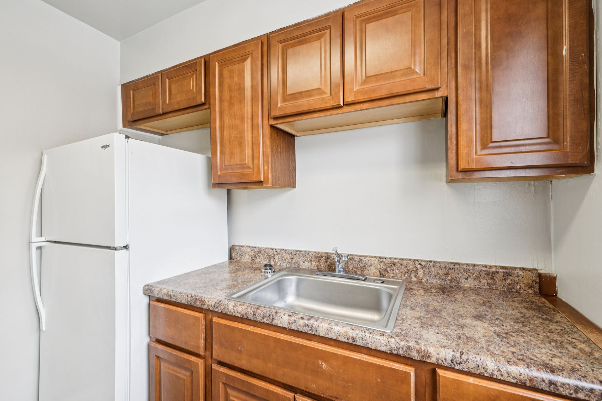 Kitchen with white refrigerator, brown cabinets, and a stainless steel sink.
