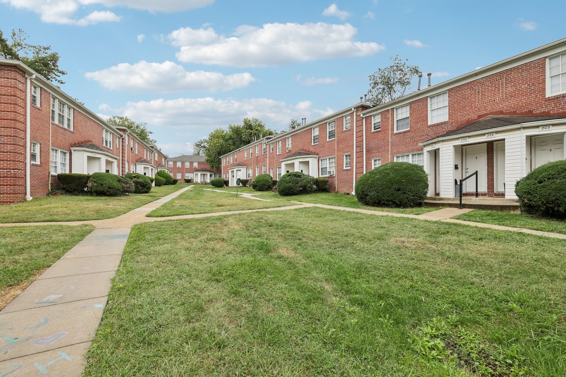 Row of brick townhouses with green lawns and sidewalks on a sunny day.