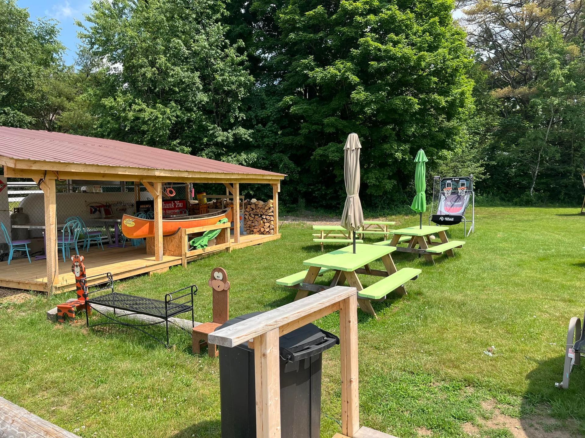 Outdoor picnic area with green picnic tables, umbrella, and shed for kayaks/canoes.