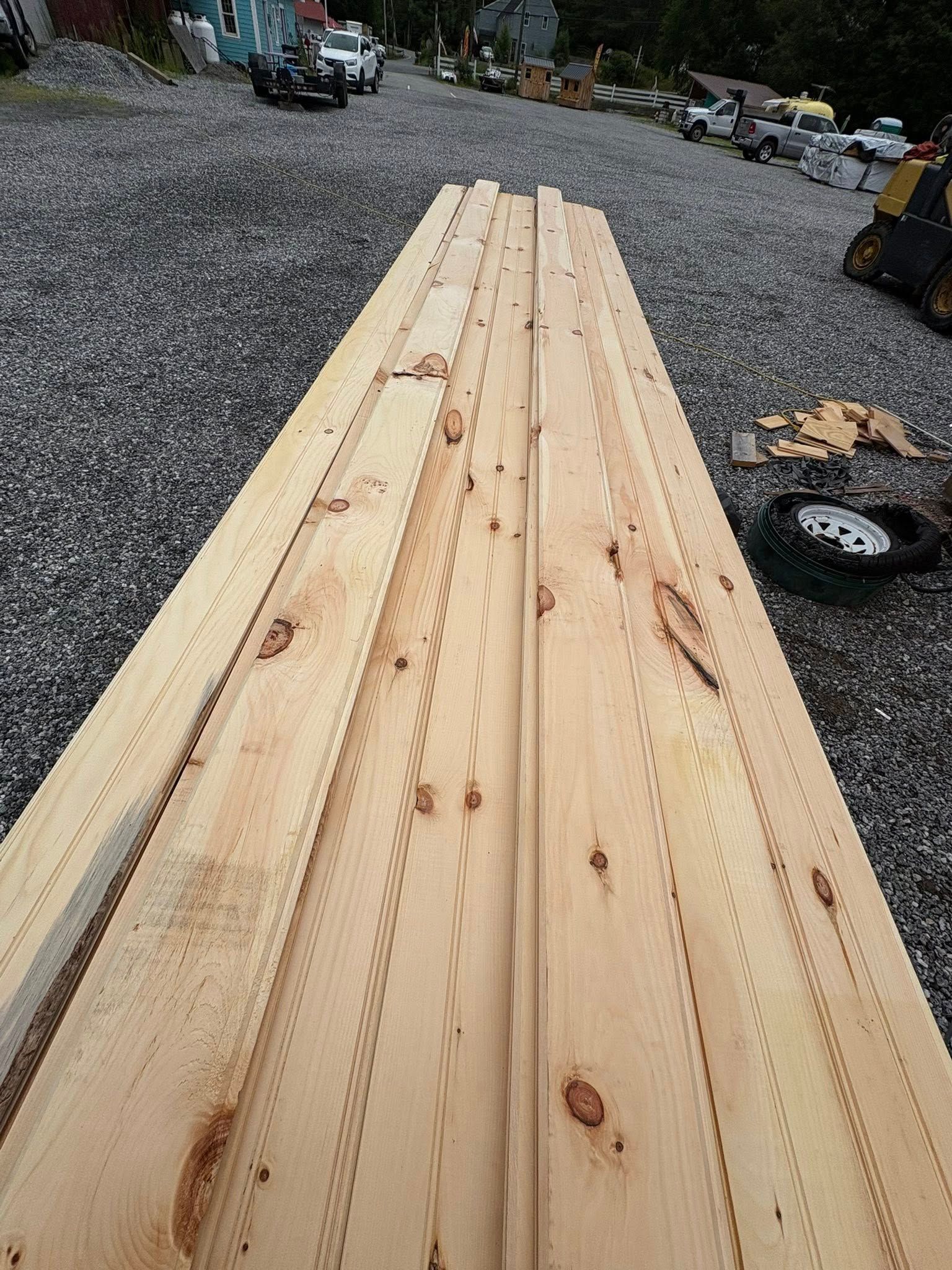 Wooden planks with grooved edges, lying on gravel, construction site background.