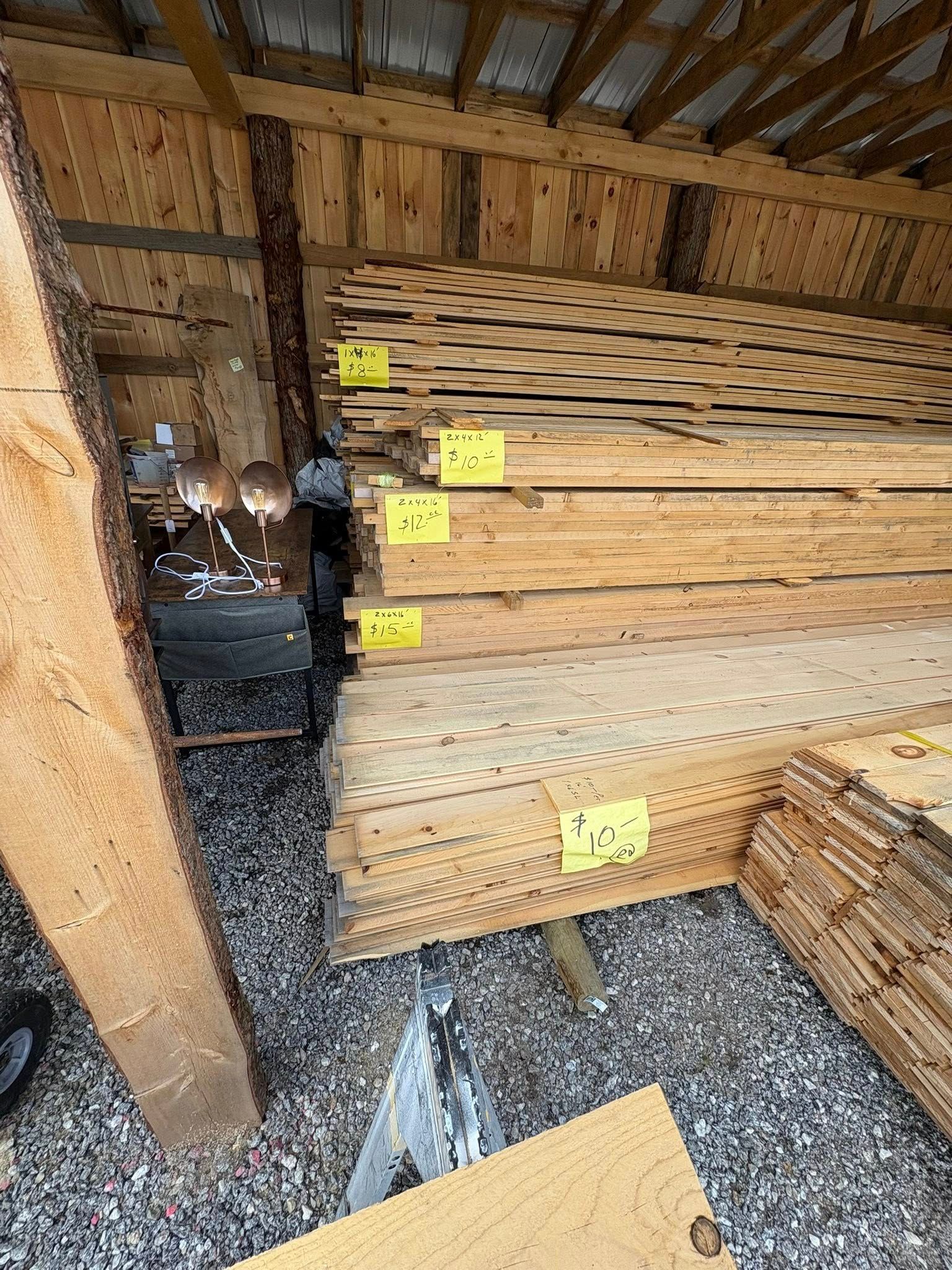 Stack of lumber with price tags in a wooden shed.