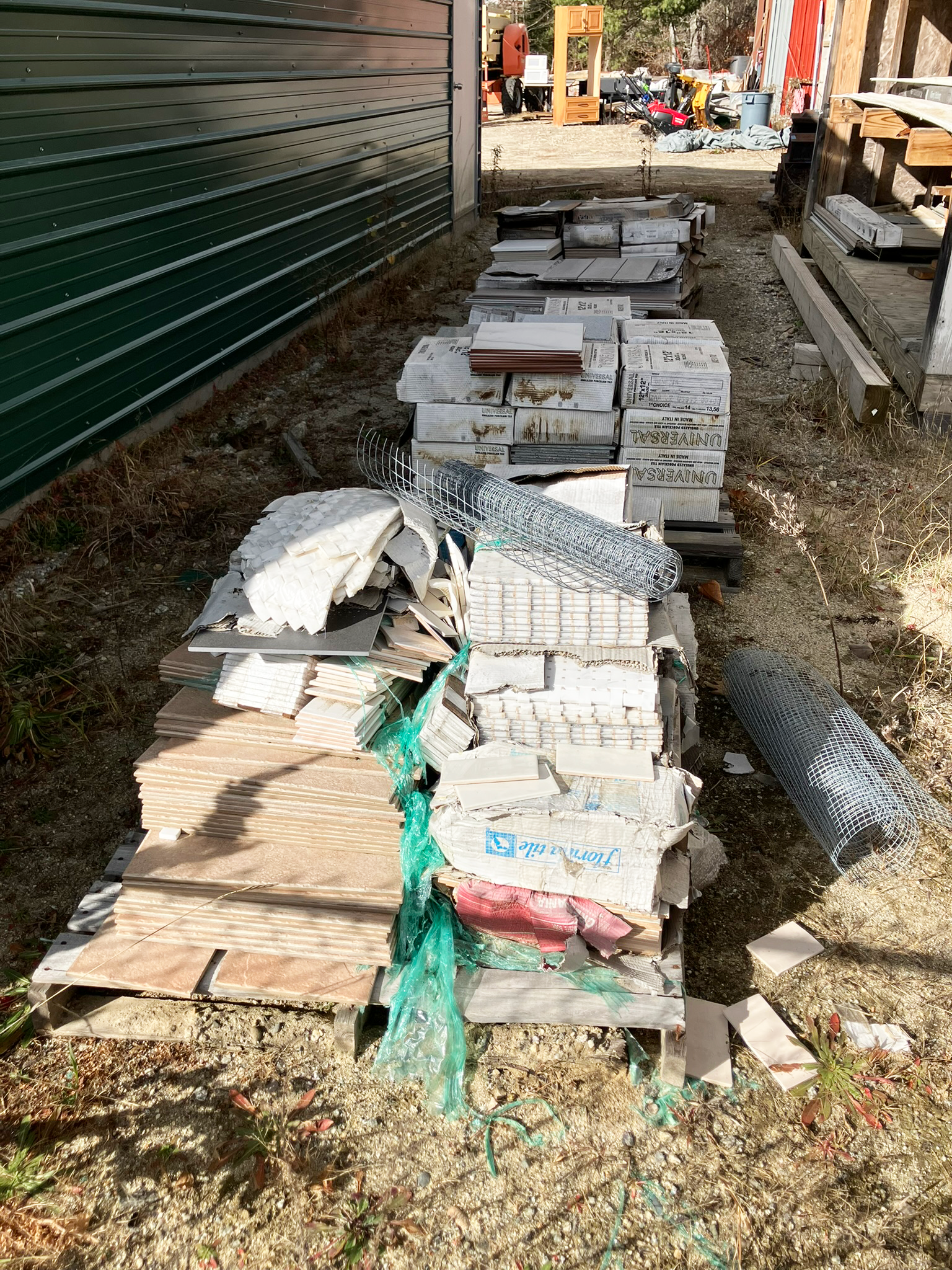 Piles of construction debris on pallets outdoors next to a green-sided building.