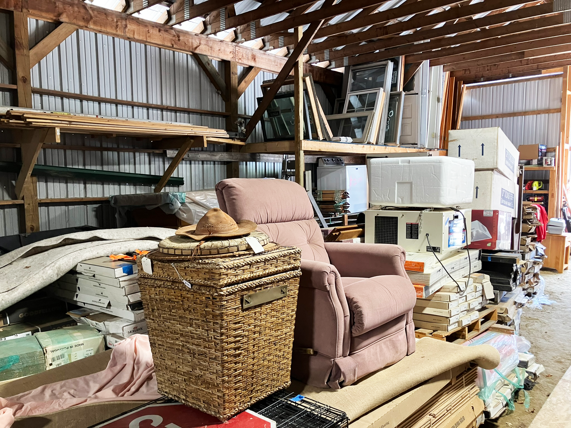 Cluttered storage area: recliner, basket with hat, stacked items, pallets, and various other objects 