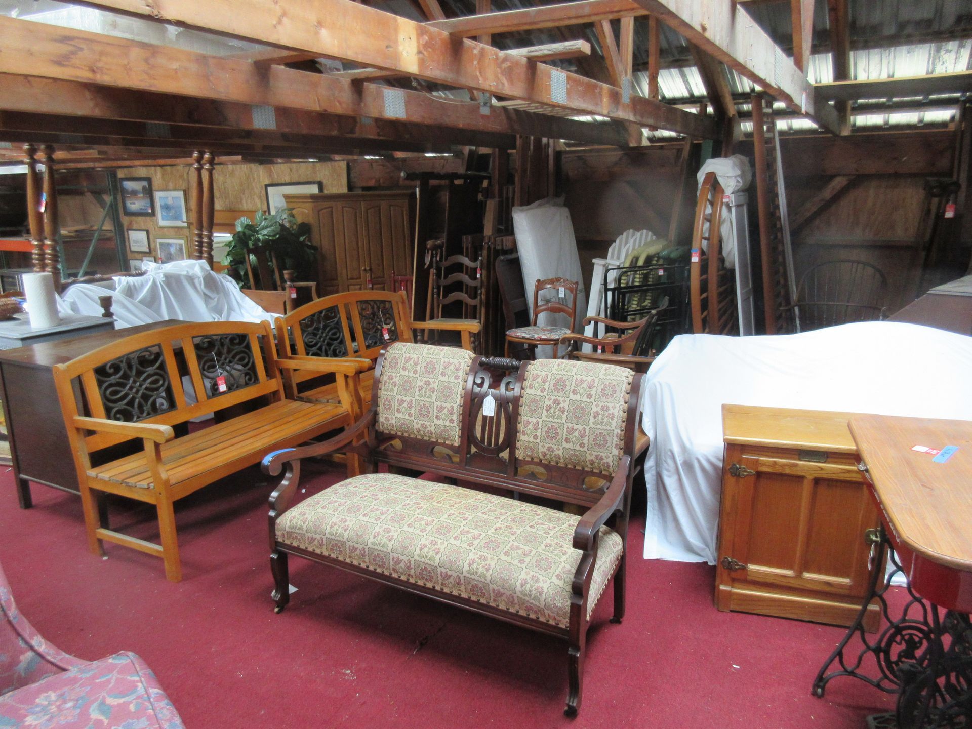 Furniture displayed inside a wooden building. Benches, tables, and cabinets sit on red carpet.