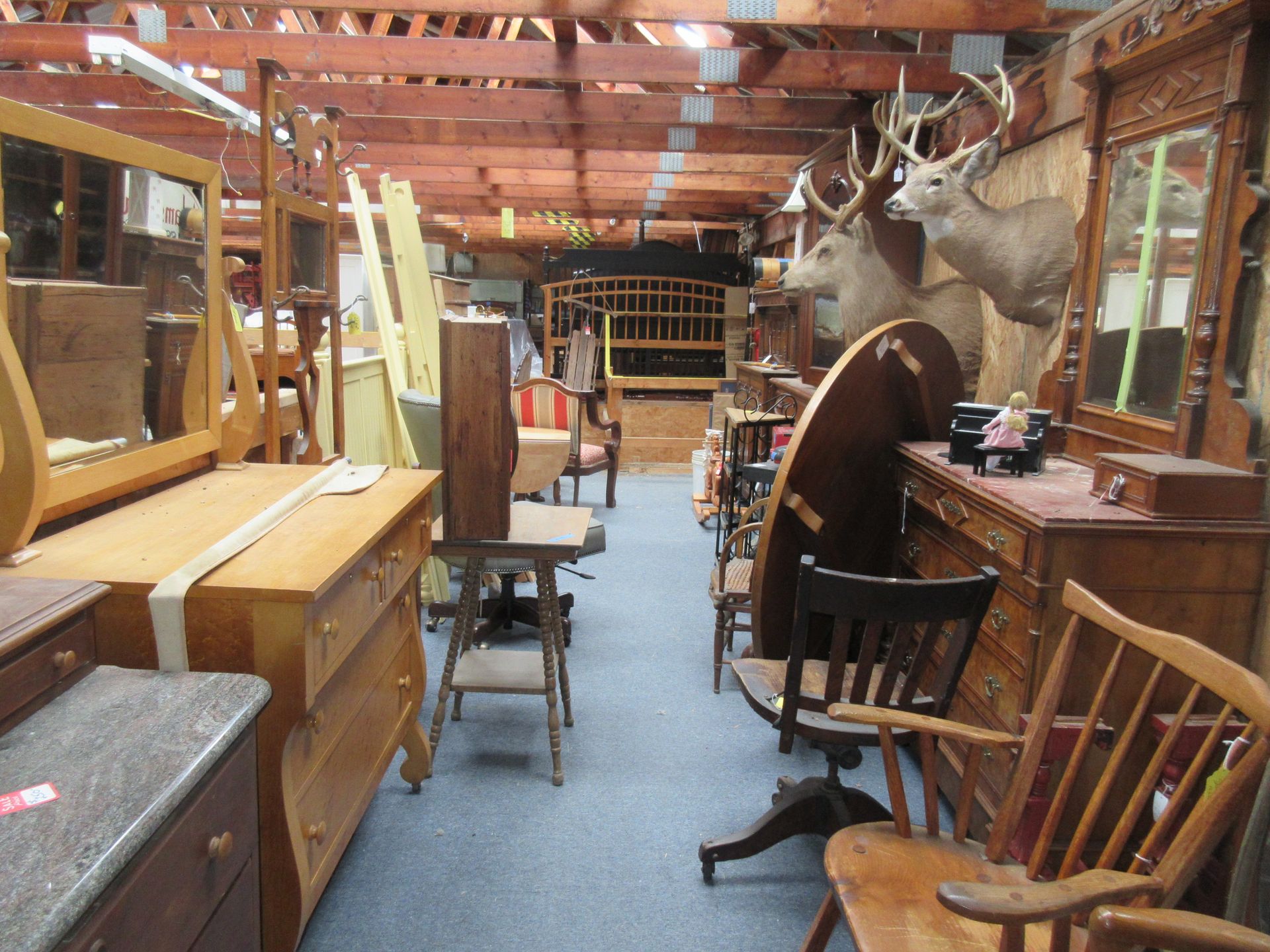 Interior of a cluttered antique store; furniture, deer heads mounted on walls, wooden beams overhead.