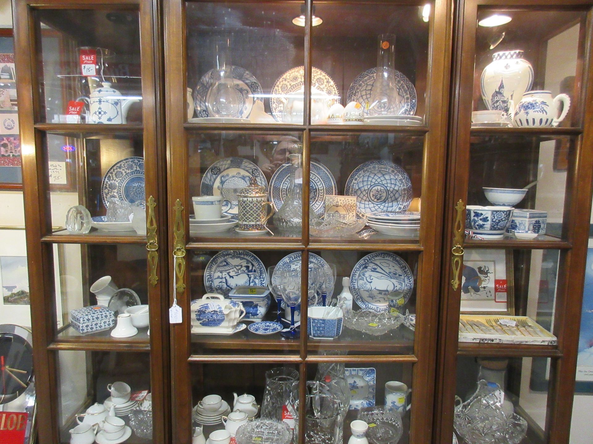 Wooden curio cabinet filled with glass and blue-and-white porcelain dishware, displayed in a shop.