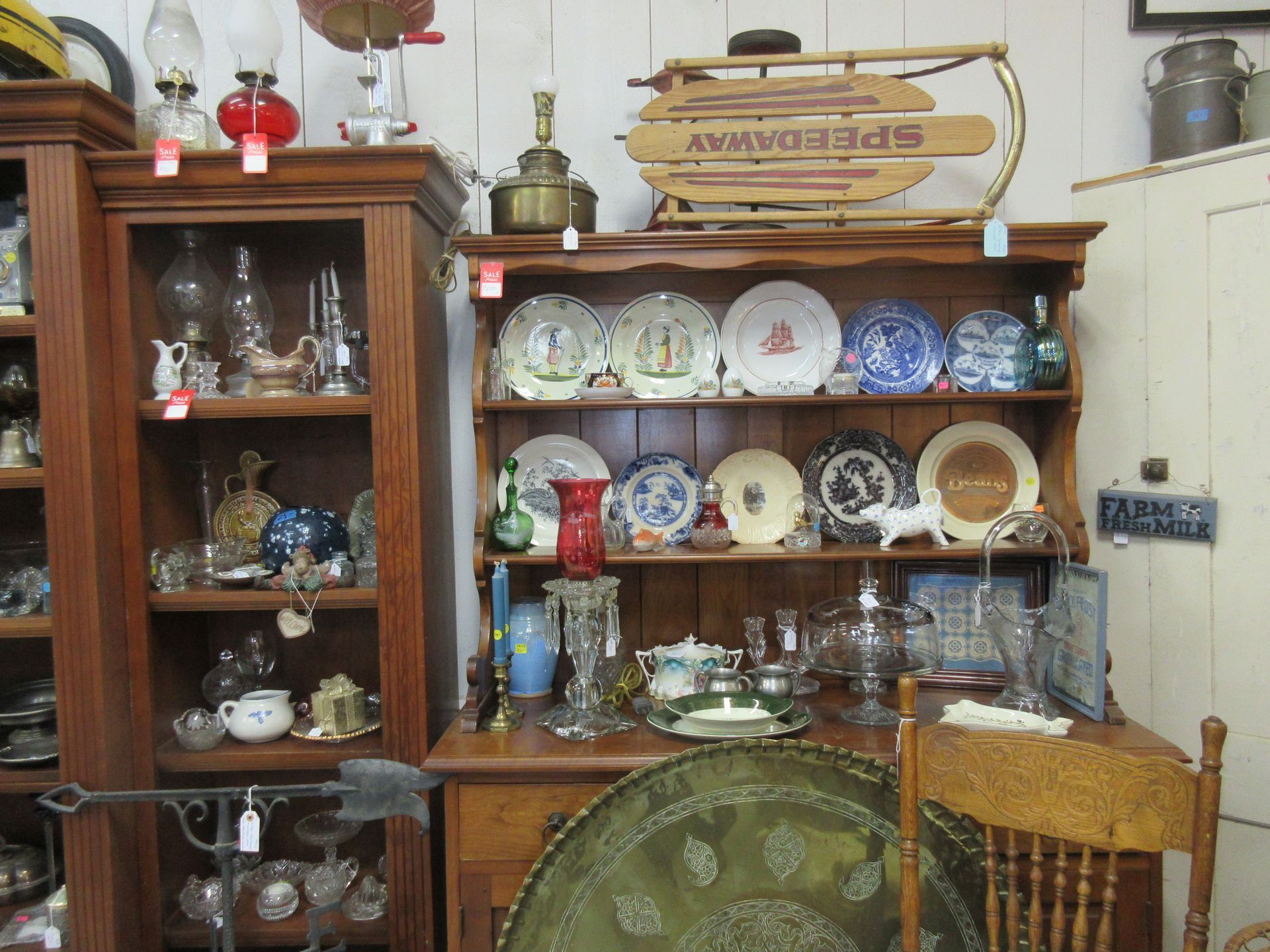 Antique shop display of dishes, lamps, and a vintage sled.