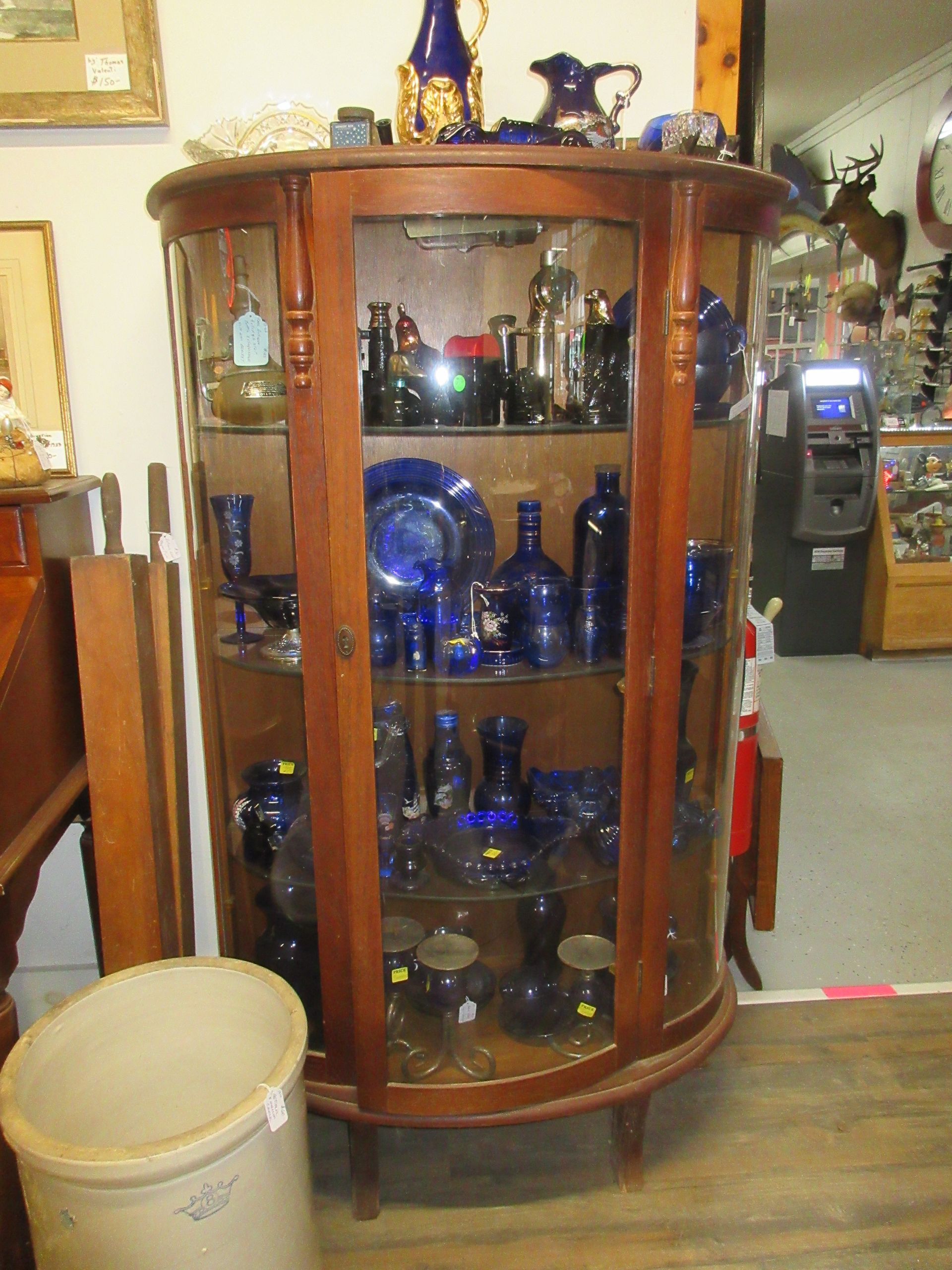 A wooden display cabinet with curved glass, filled with blue glassware in a shop setting.