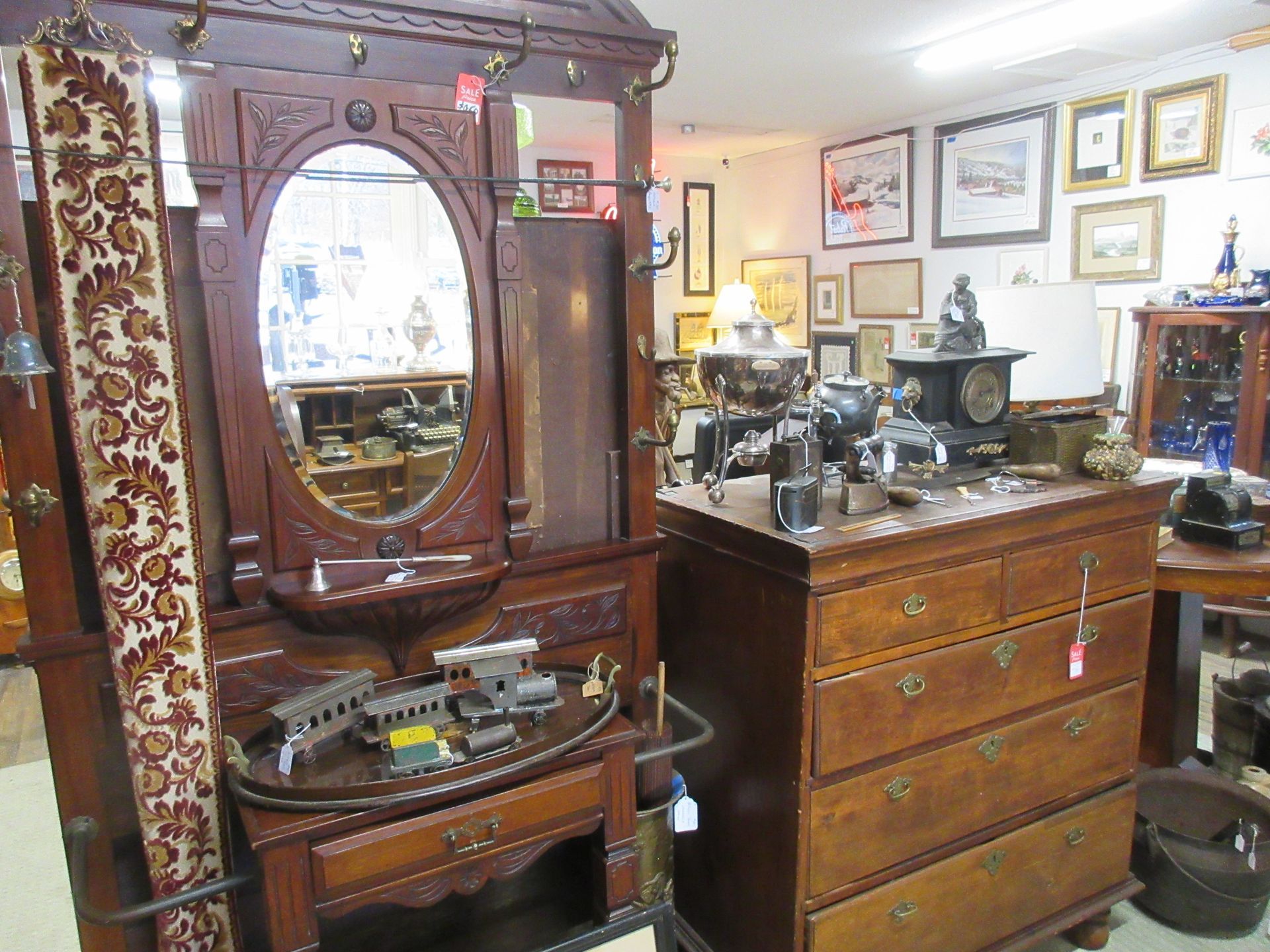 Antique furniture in a shop, including a hall tree with a mirror and a wooden chest of drawers.
