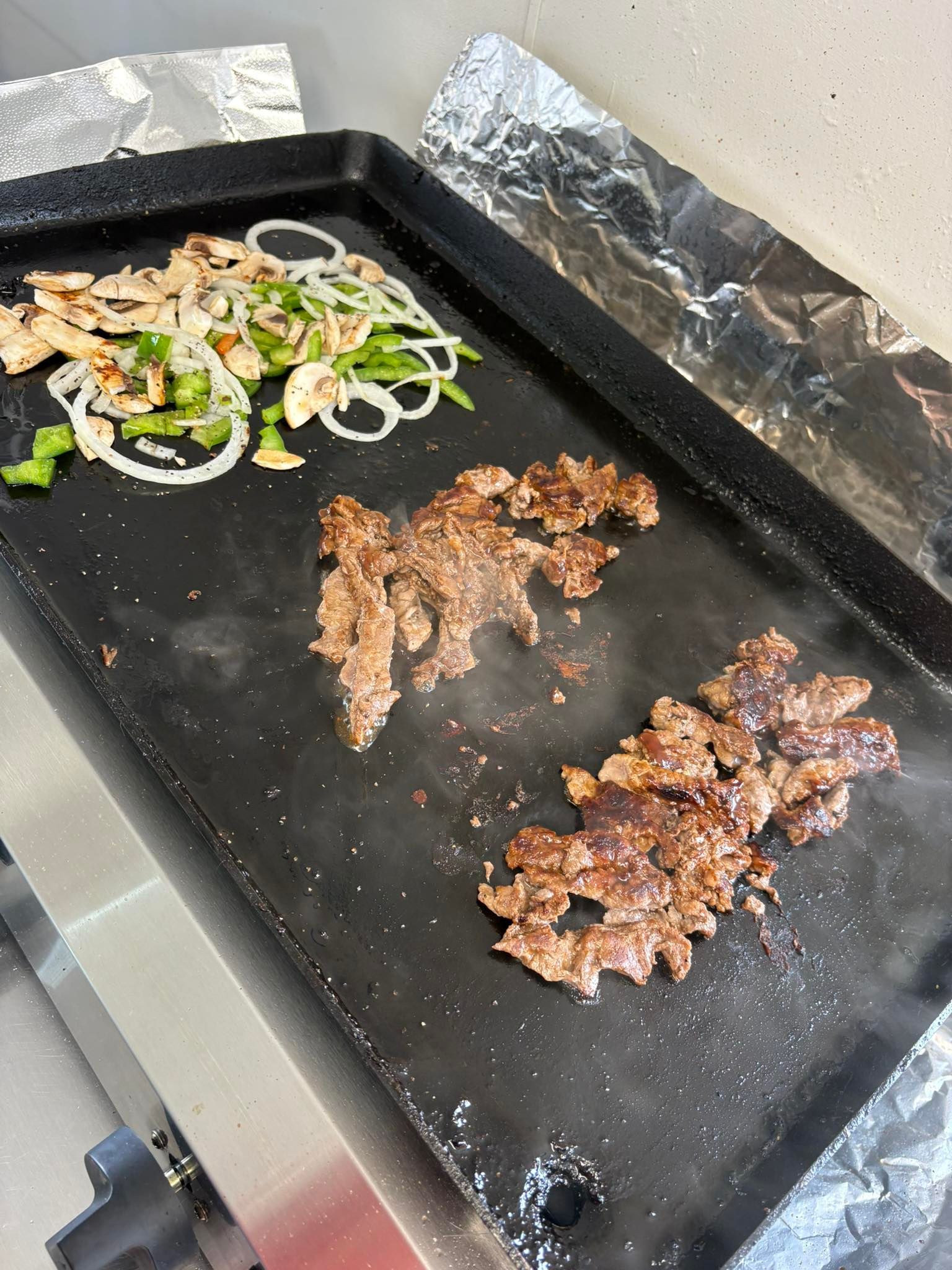 Meat and vegetables cooking on a black griddle.