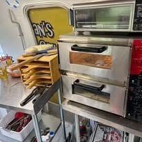 A commercial kitchen setup, with a pizza oven, shelves for pizza peels, and various cooking tools.