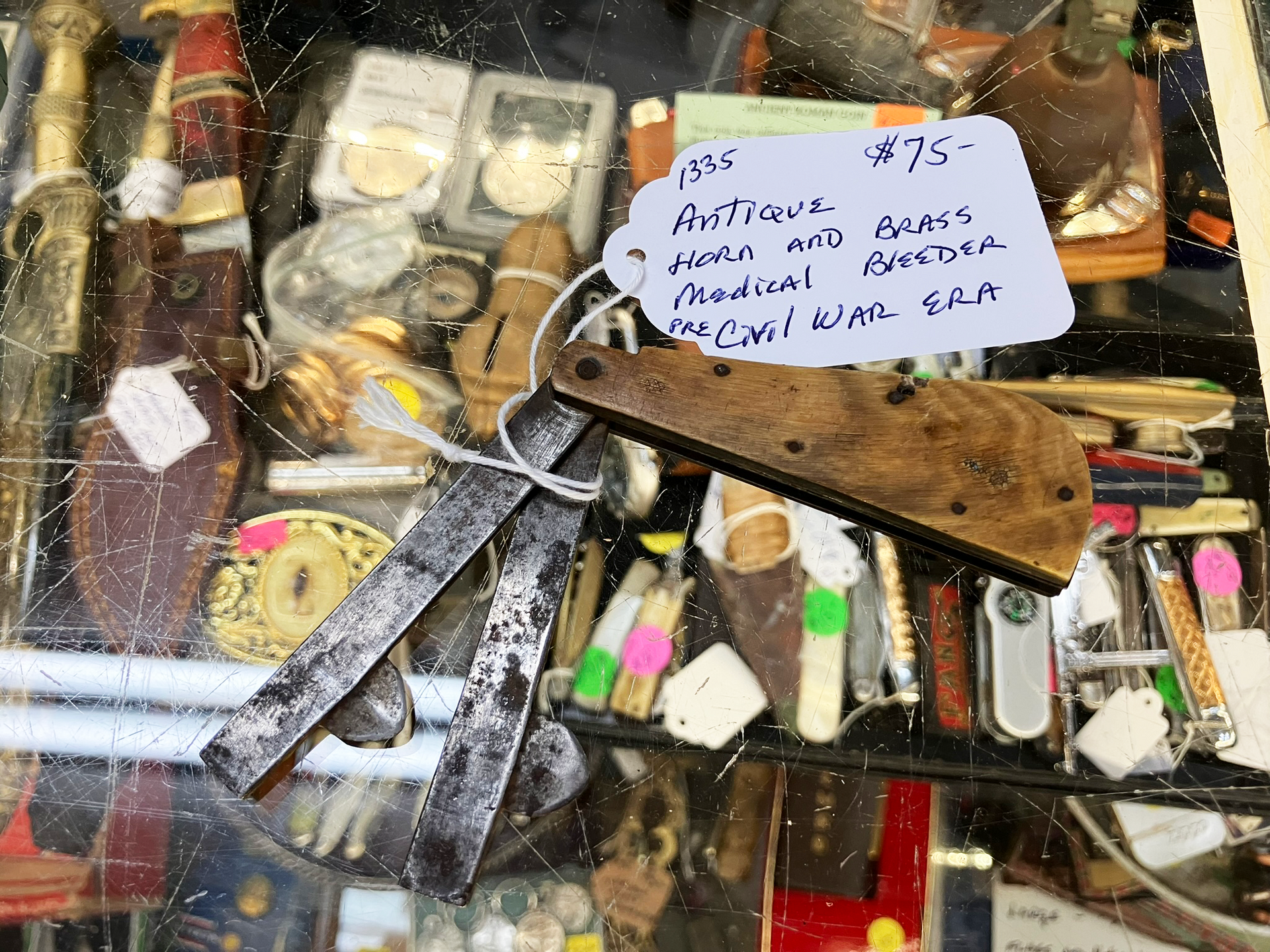 Antique pocket knife and blades with price tag in a display case.