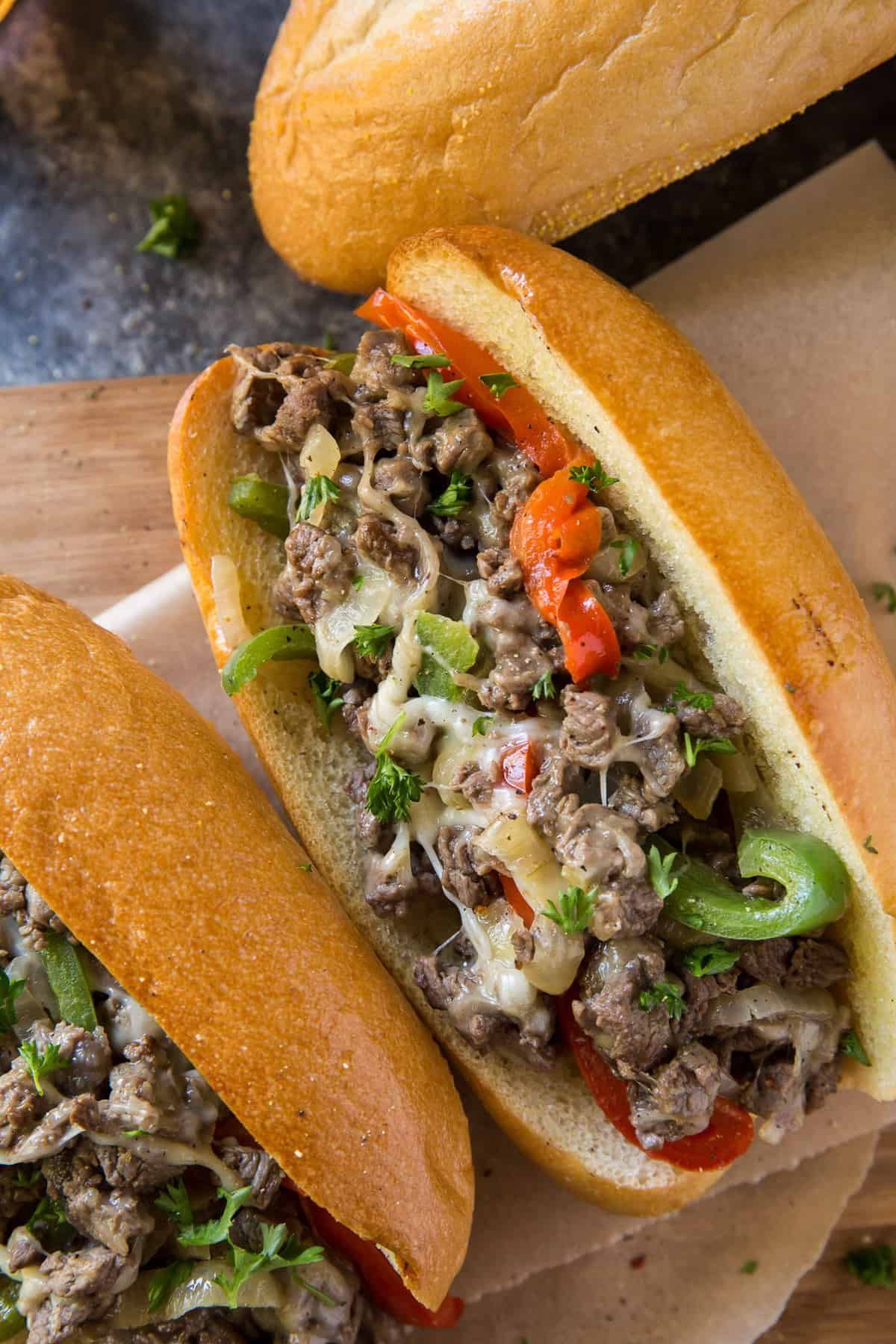 Cheesesteak sandwiches with peppers, onions, and cheese in toasted sub rolls, close-up.