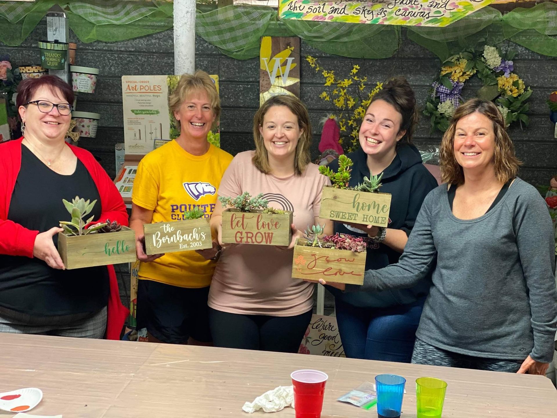 A group of women are standing around a table holding potted plants.