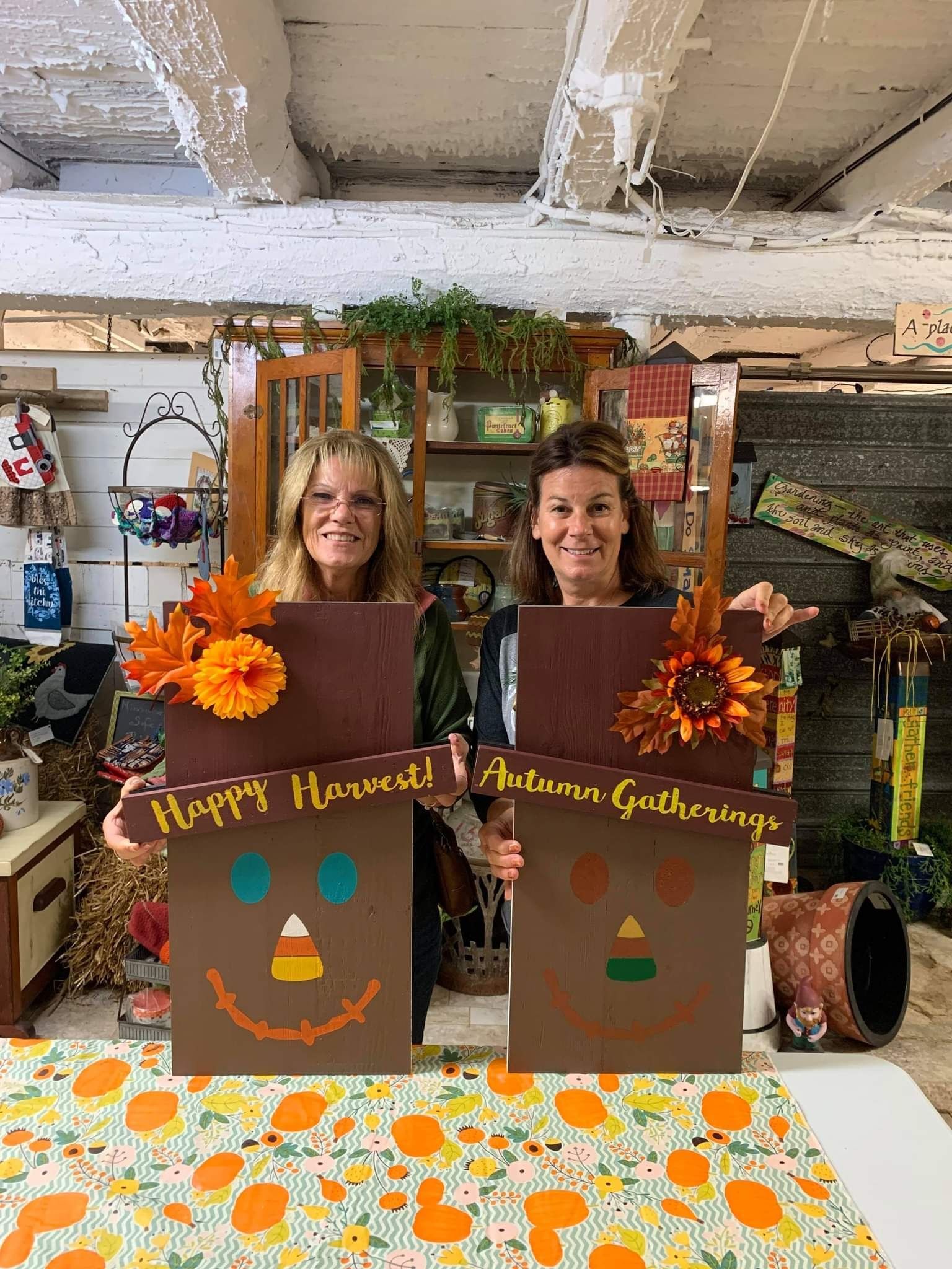 Two women are standing next to each other holding a sign that says `` happy autumn gathering ''.