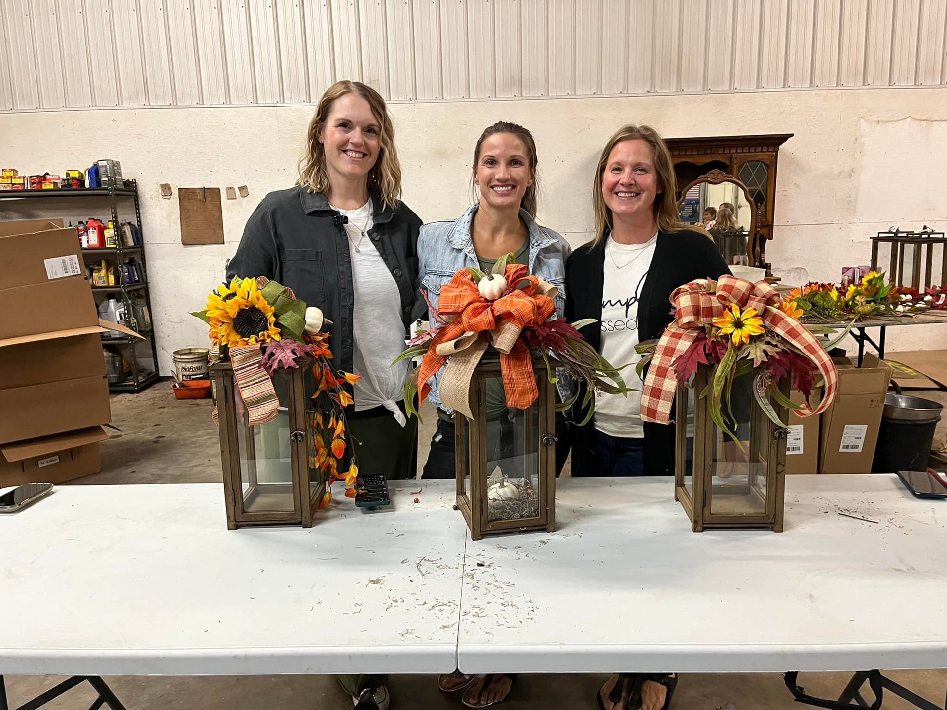 Three women are standing next to a table with lanterns decorated with flowers.