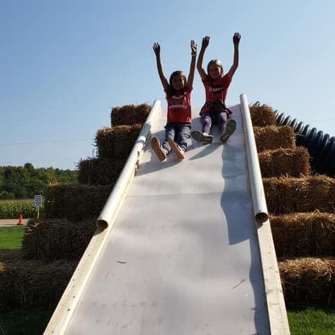 Two young girls are sitting on a slide made of hay bales.