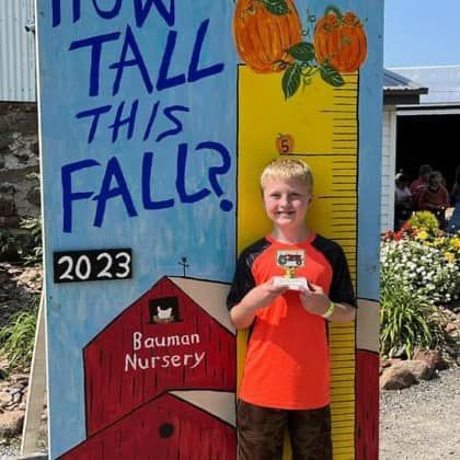 A young boy is standing in front of a sign that says `` how tall this fall ''.