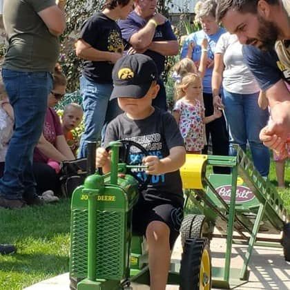 A young boy is riding a toy tractor in front of a crowd of people.