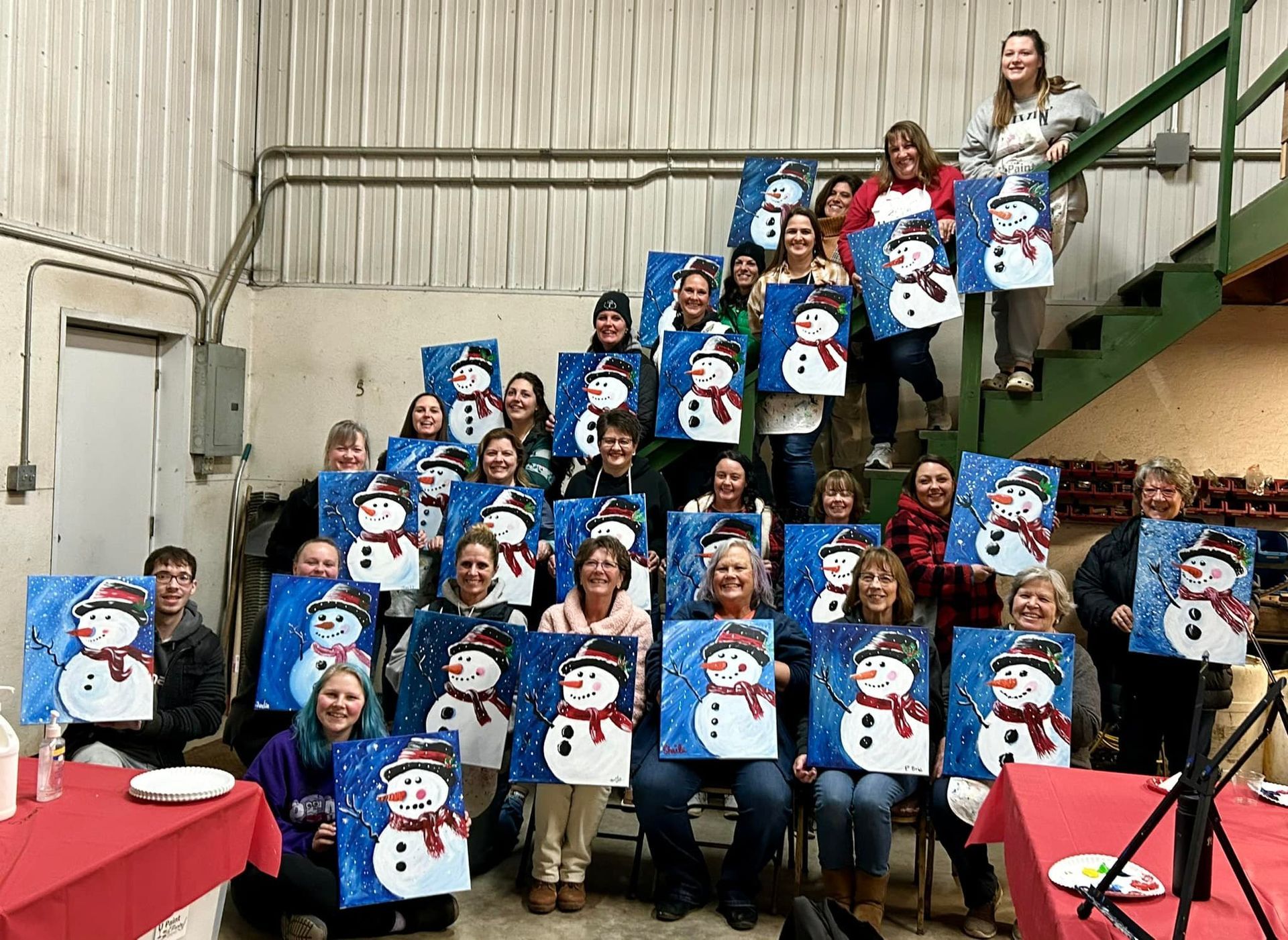 A group of people are posing for a picture while holding paintings of snowmen.