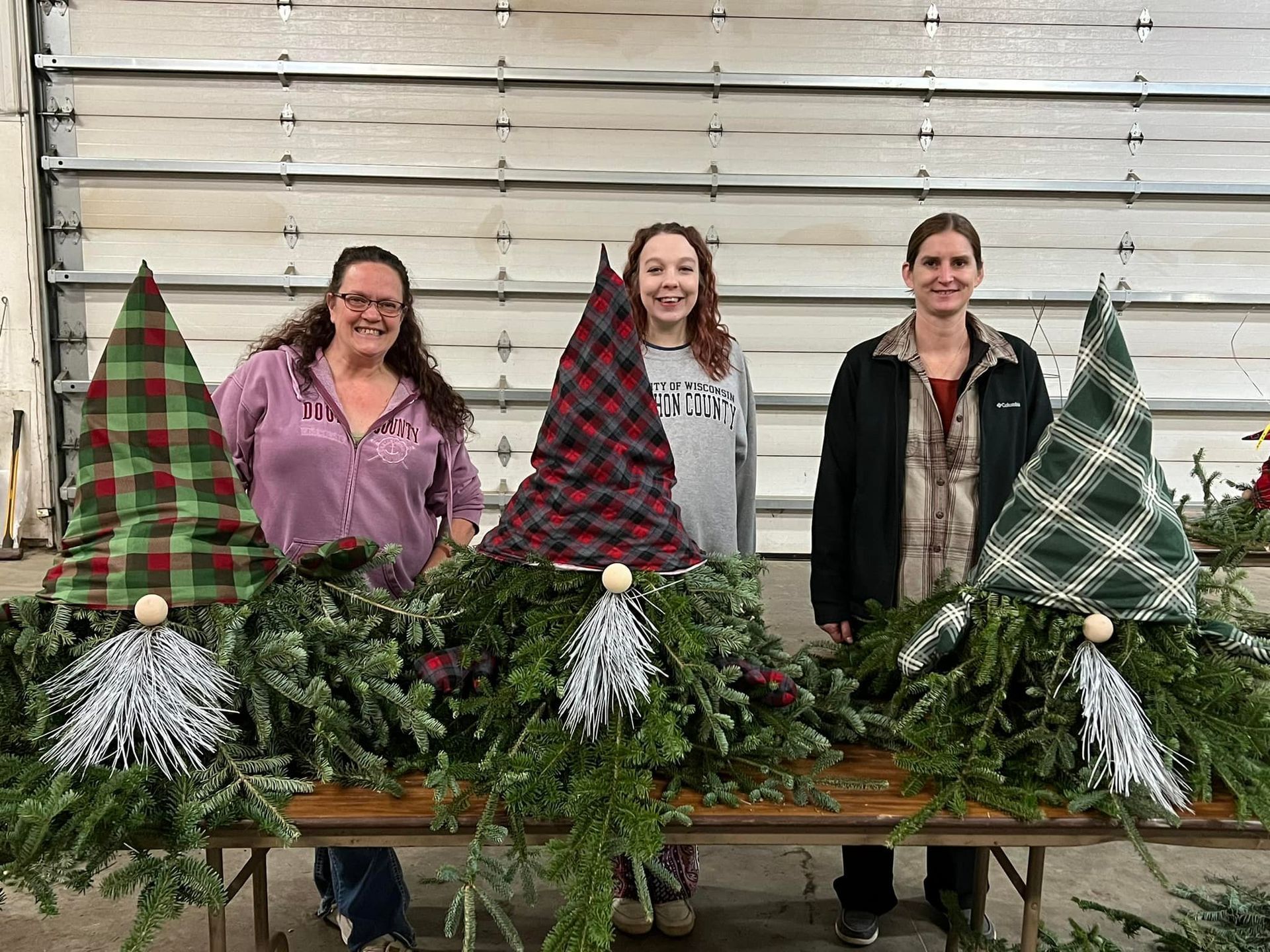 Three women are standing next to a table with gnome hats on it.