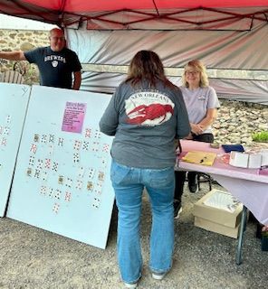 A woman wearing a gray shirt with a lobster on it is standing in front of a table.
