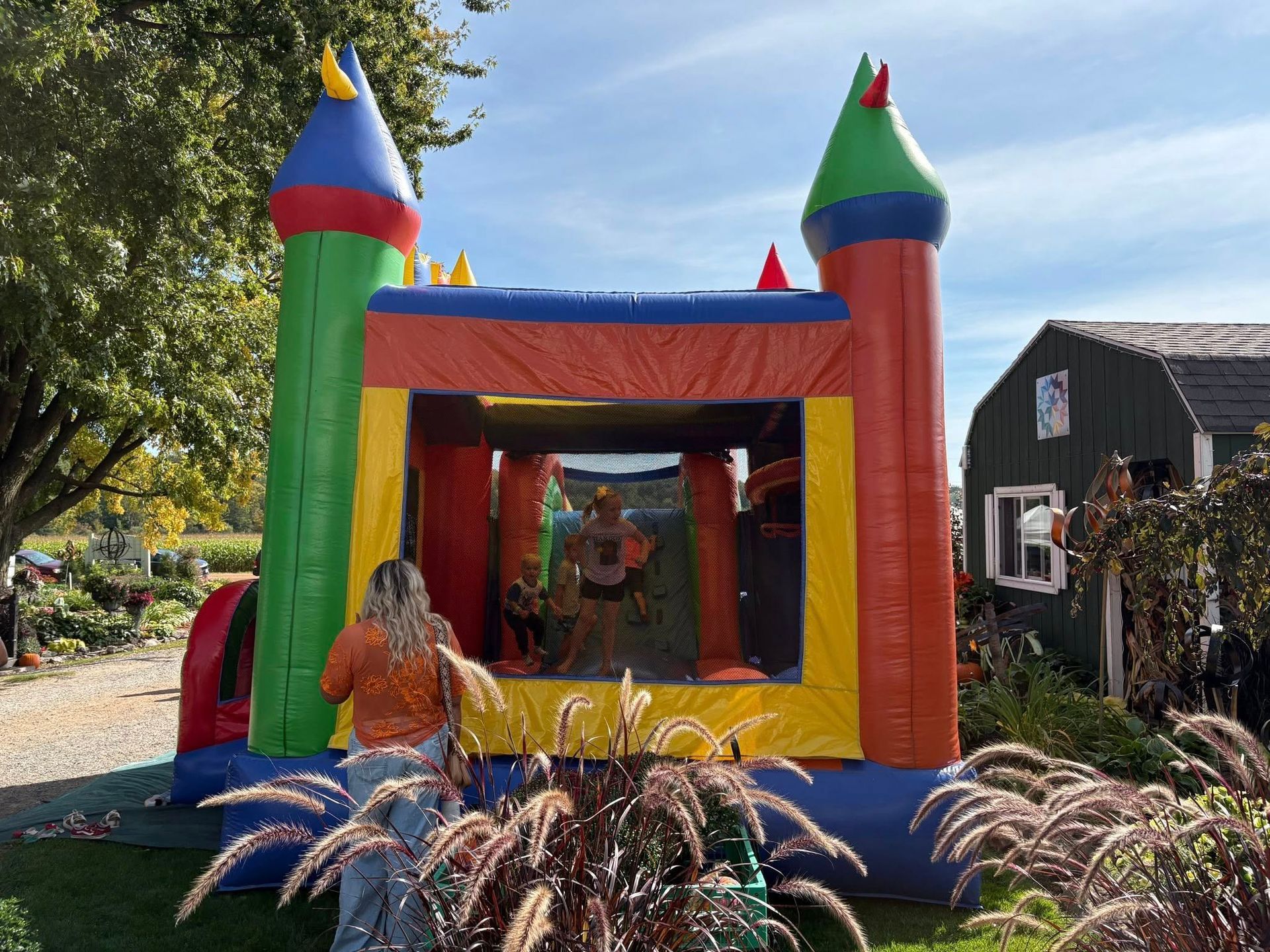 Colorful bounce house with two people, plants, and a building on a sunny day.