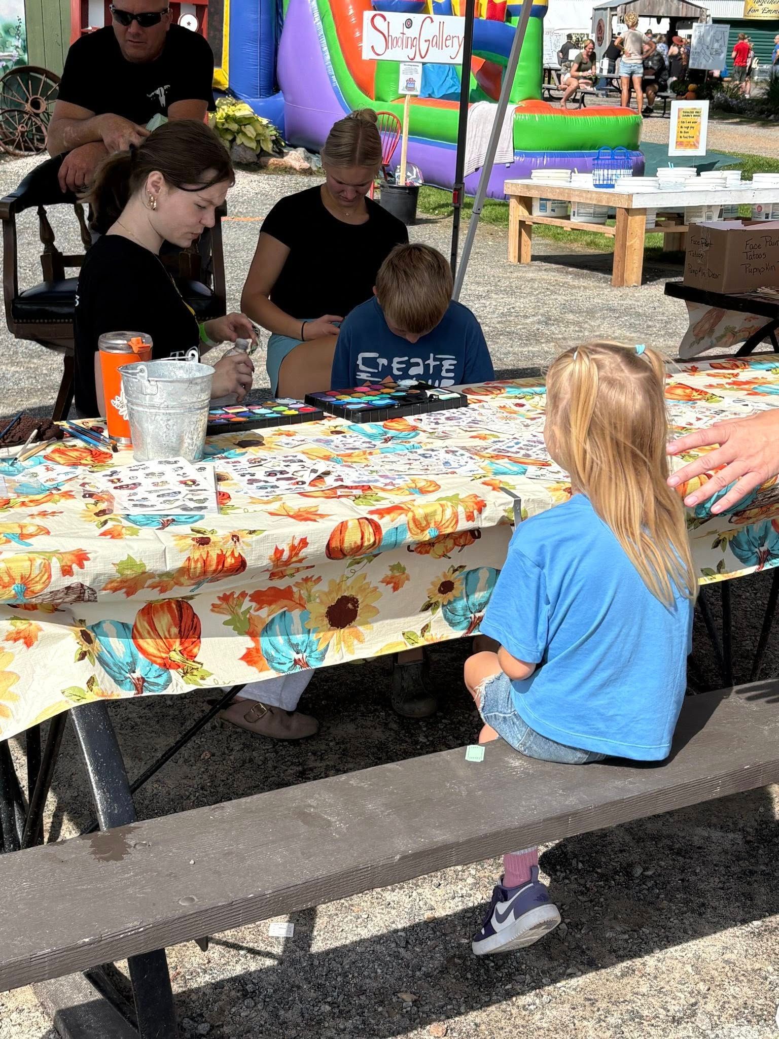 People at a table doing crafts outdoors, with a bouncy house in the background.