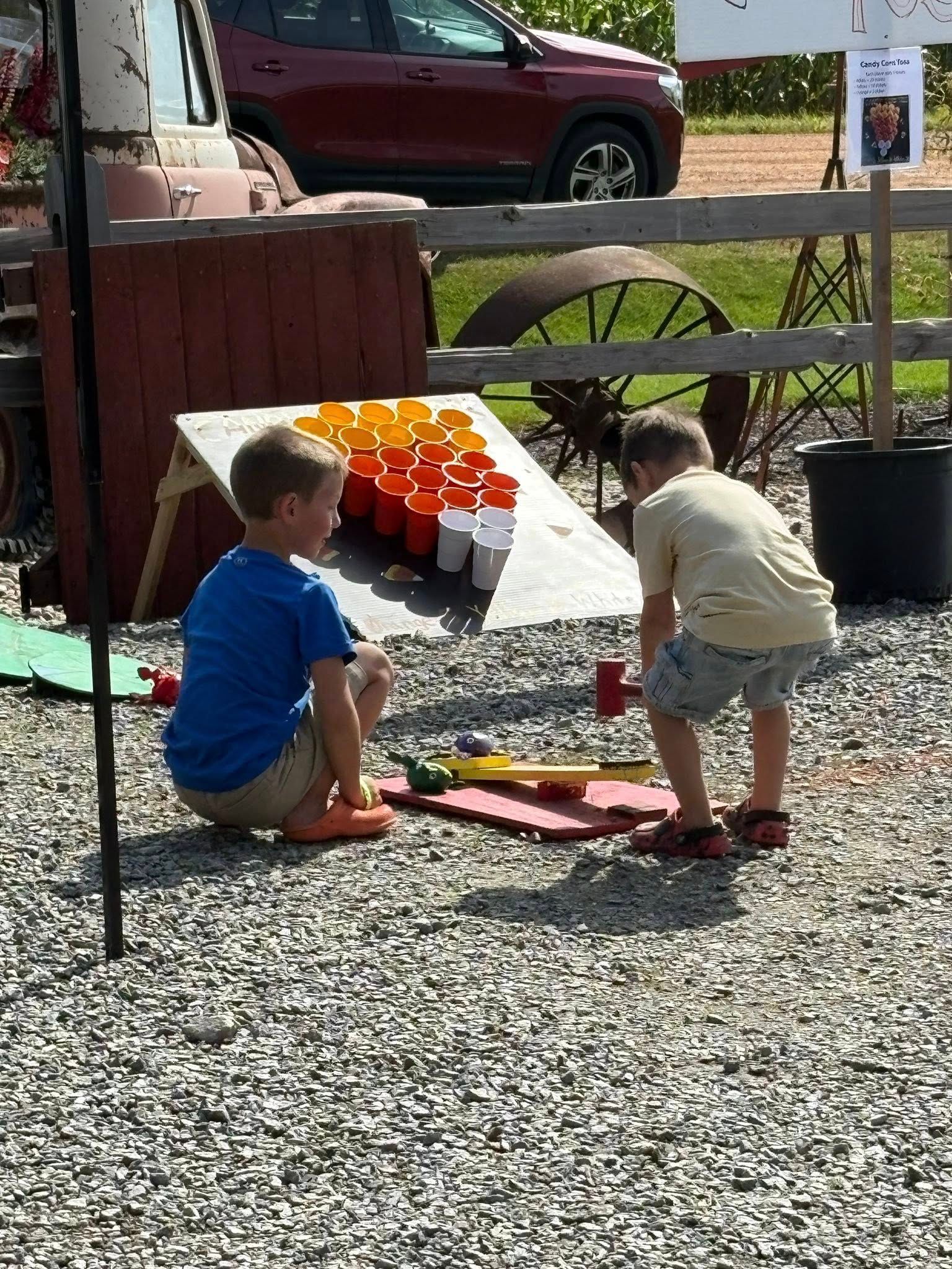 Two children playing a game at an outdoor event with red, orange cups set up on a slanted wooden surface.