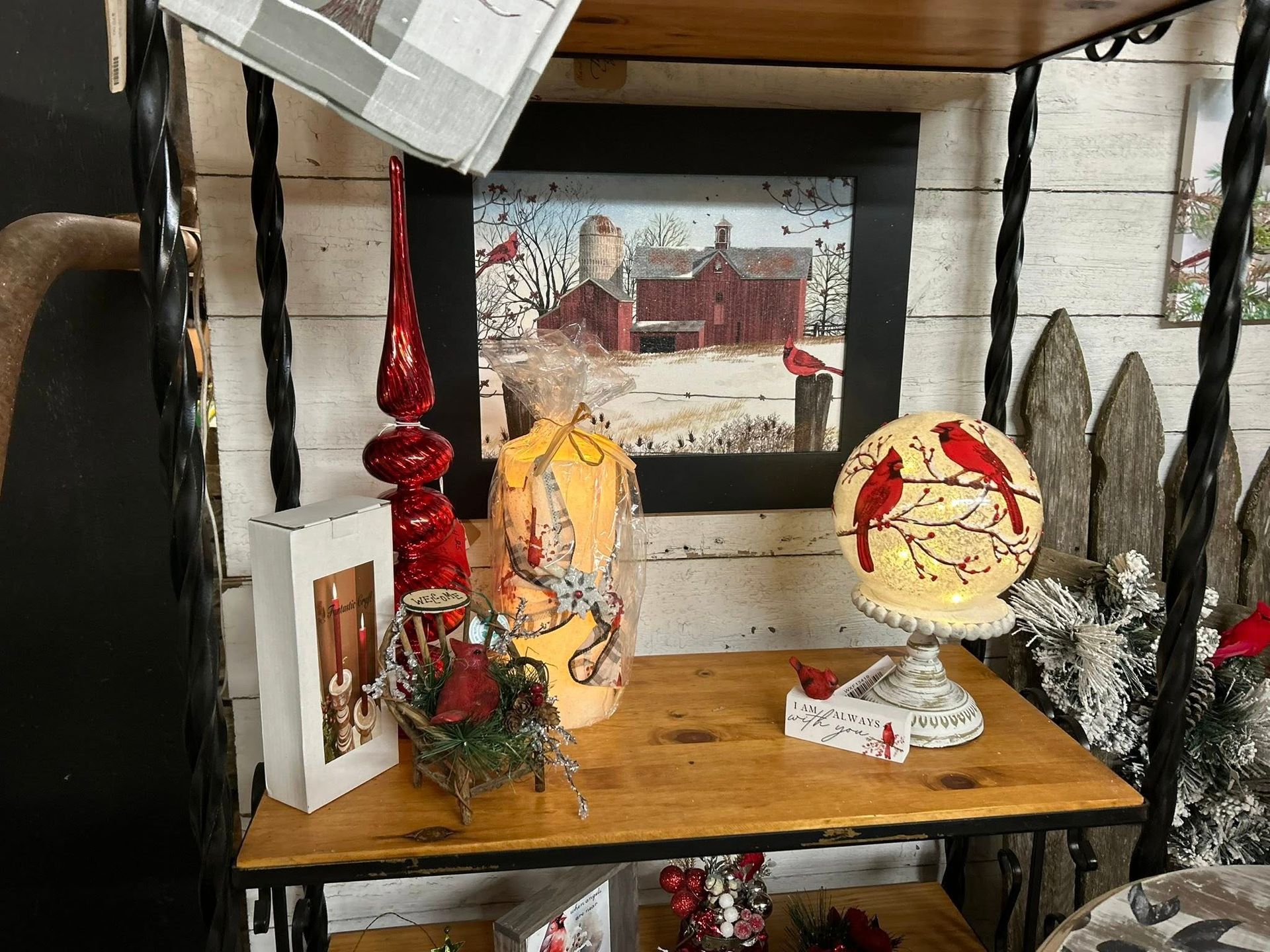 Wooden shelf with winter-themed decorations: painting, cardinal lamp, red ornaments, and snow-covered greenery.