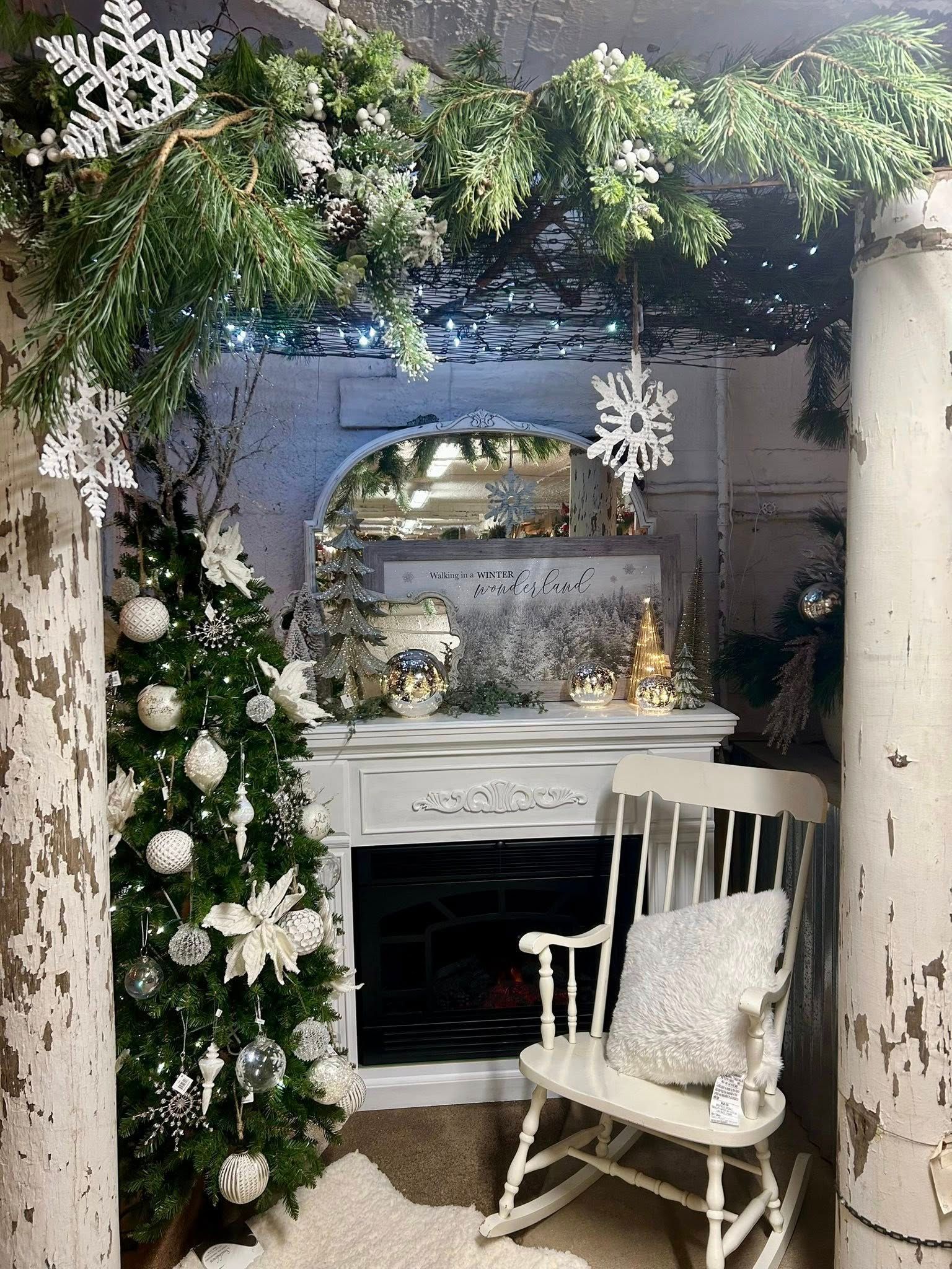 Cozy winter scene: White fireplace, Christmas tree, rocking chair, and decorations in a rustic setting with greenery and snowflakes.