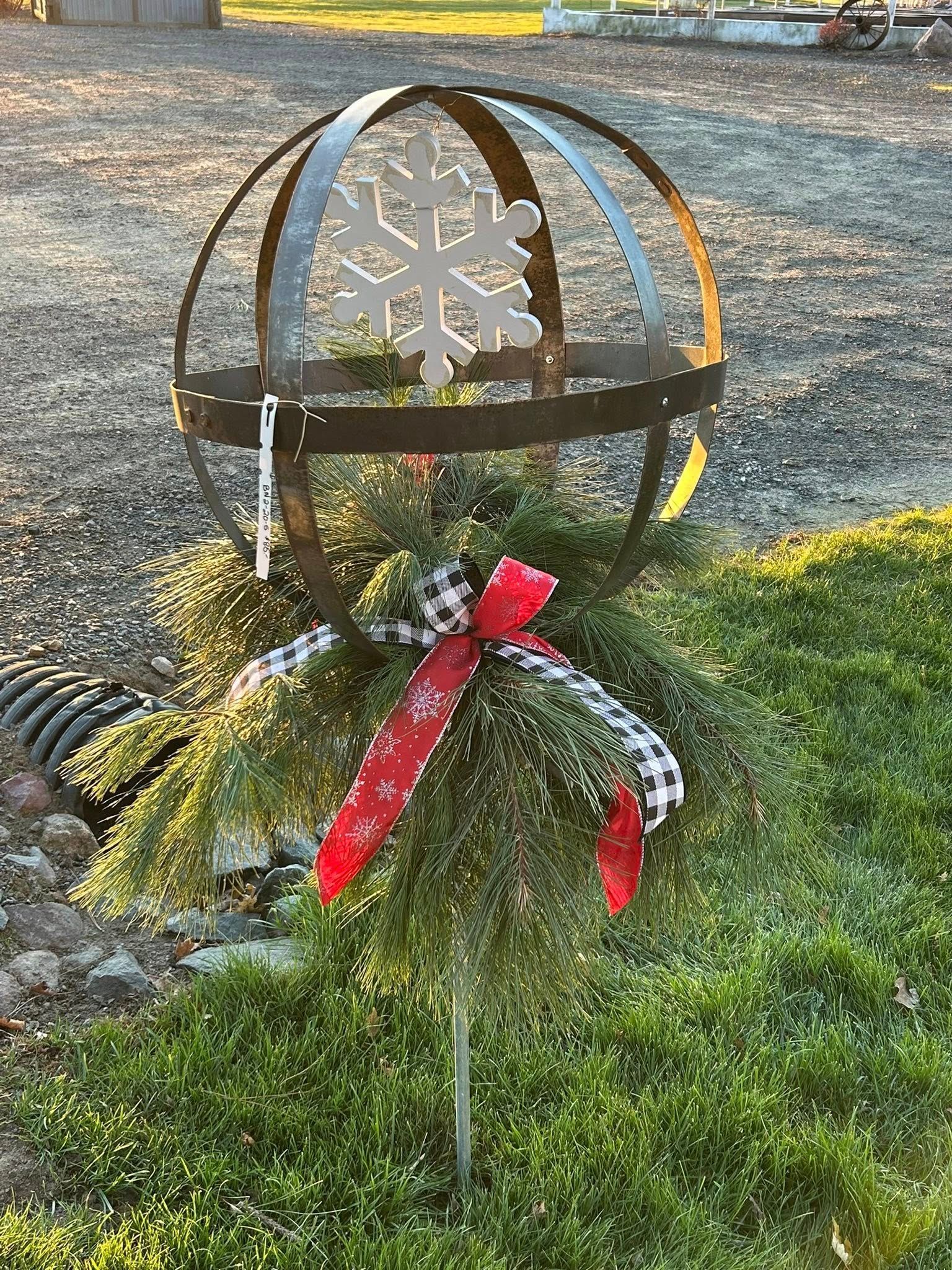Metal sphere yard decoration with snowflake and ribbon on evergreen foliage.