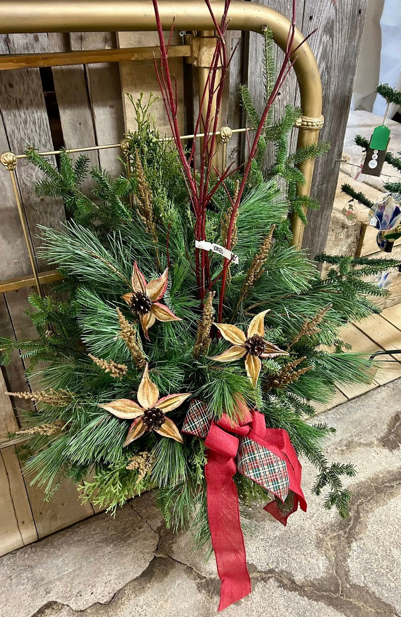 Christmas floral arrangement: evergreen boughs, gold star-shaped ornaments, red ribbon.