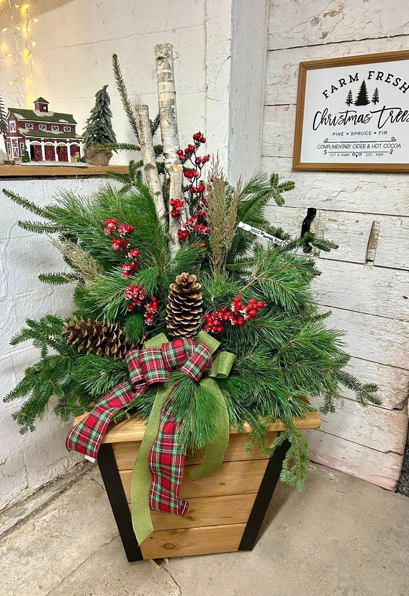 Holiday floral arrangement in a wooden container with greenery, berries, pinecones, and plaid ribbon.