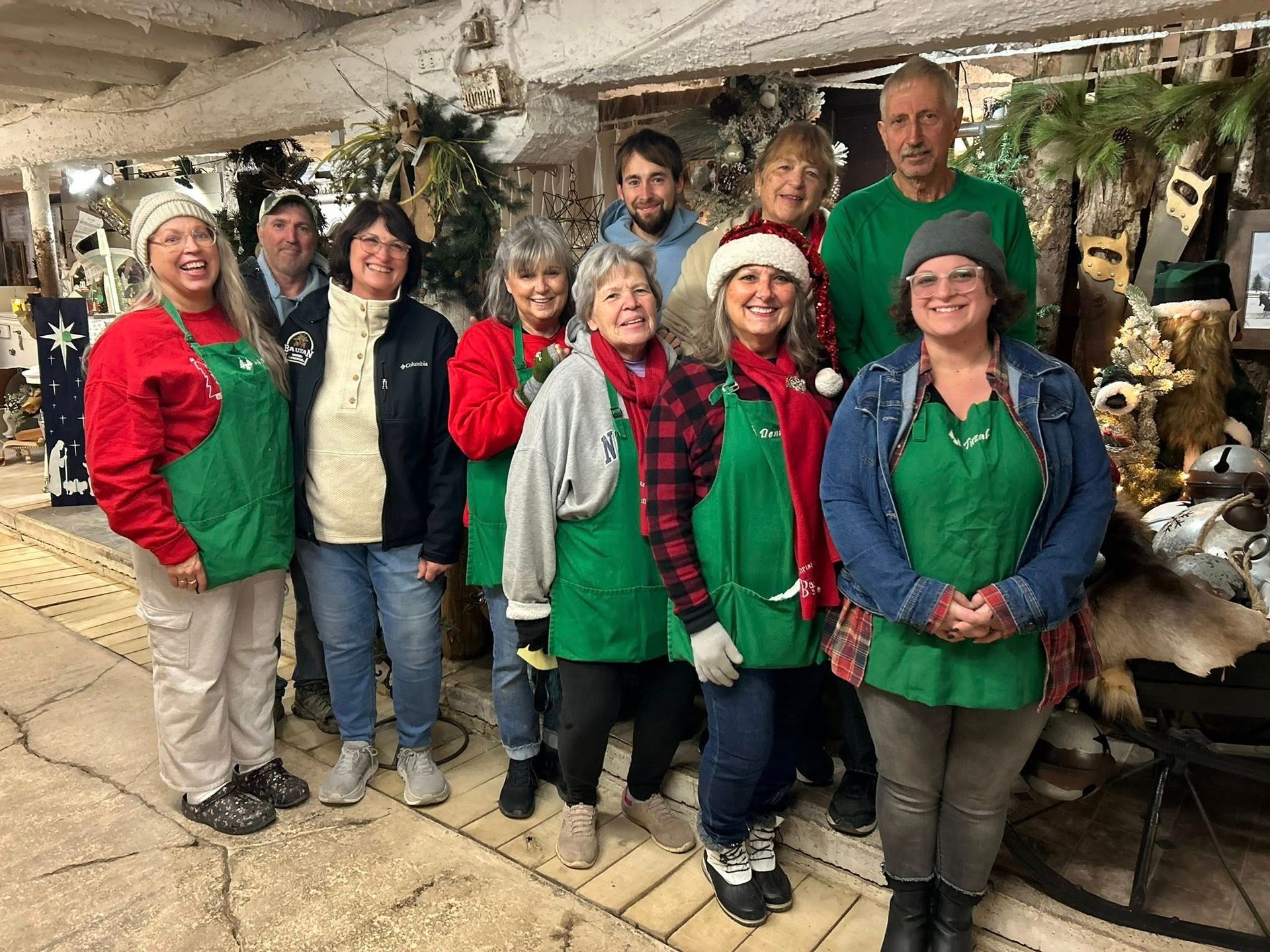 Group of people wearing green aprons and Christmas attire, posing indoors.