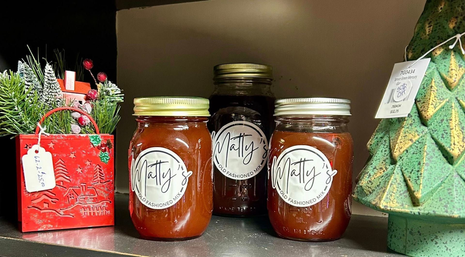 Three jars of food with labels on a shelf, next to holiday decorations.